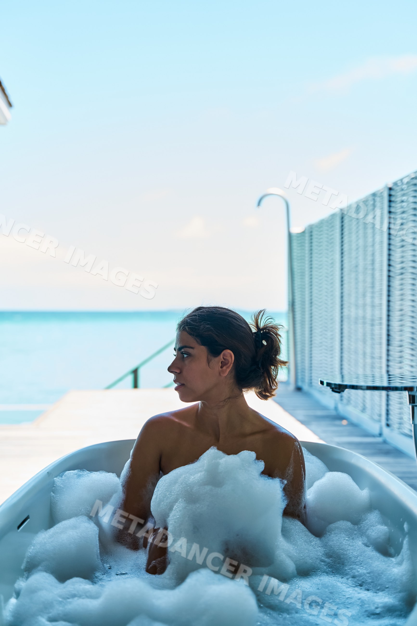 A white woman relaxes in a bubble bath with an ocean view