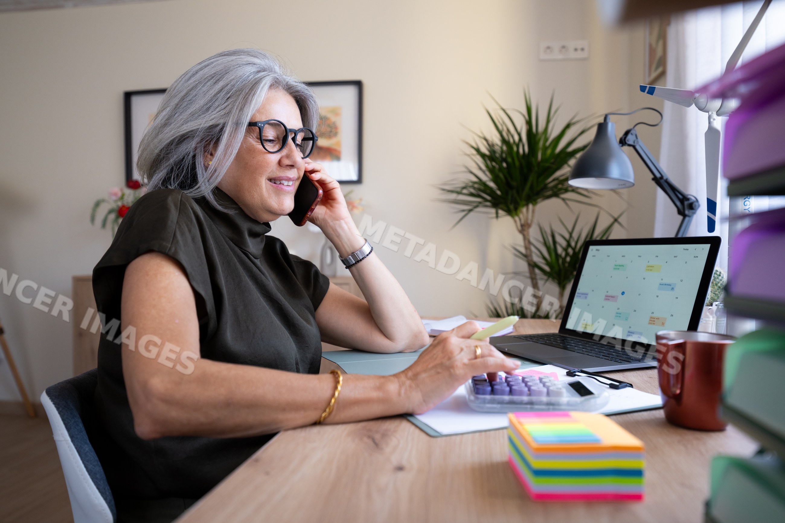 White woman multitasking with phone and calculator at home office desk
