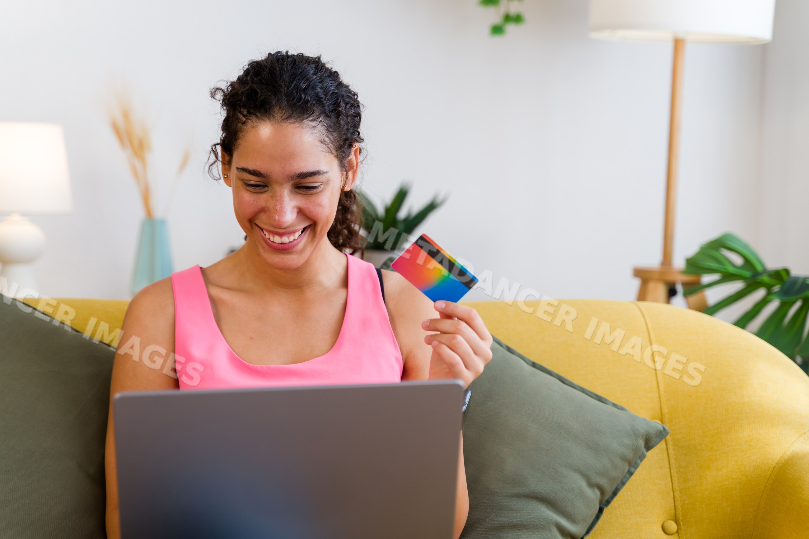 A Hispanic woman happily shops online using a credit card and laptop