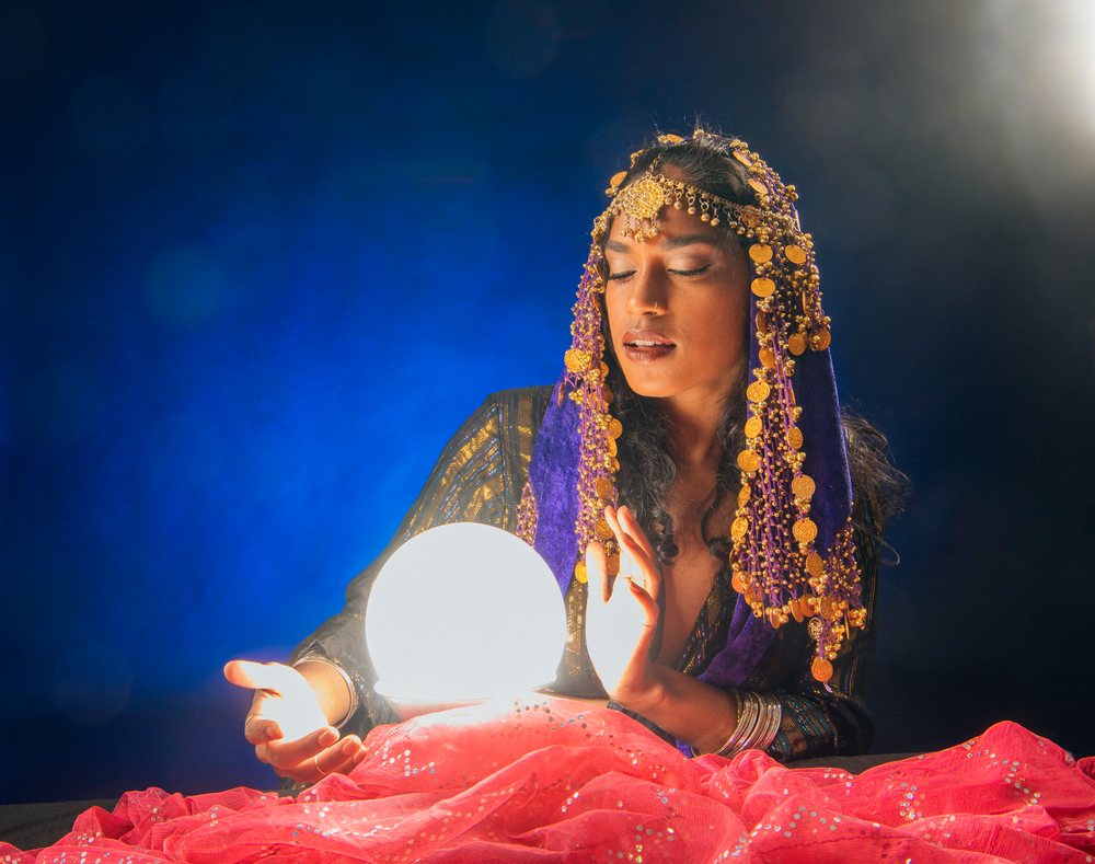 A South Asian woman acts as a fortune teller with a glowing crystal