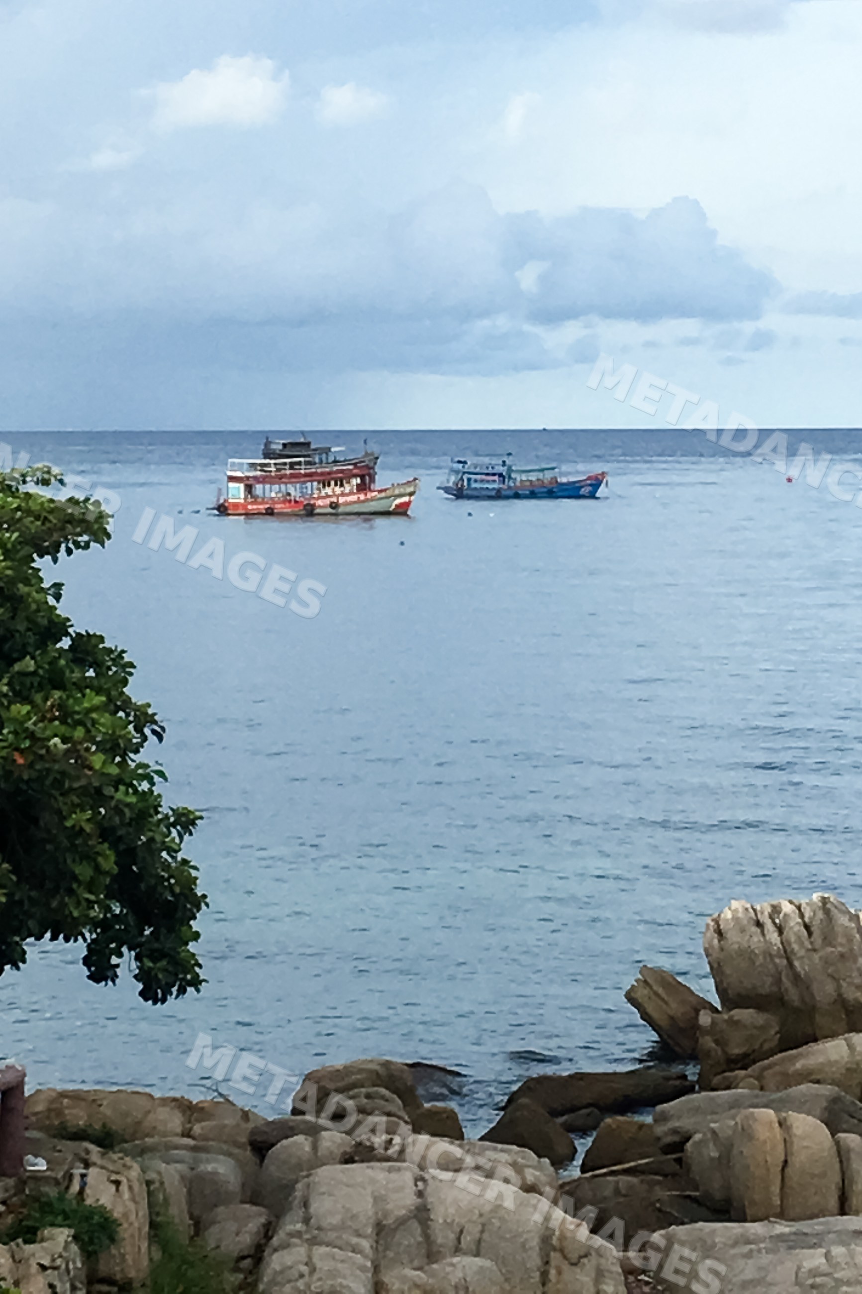 Boats float on sea near rocky shoreline in Philippines