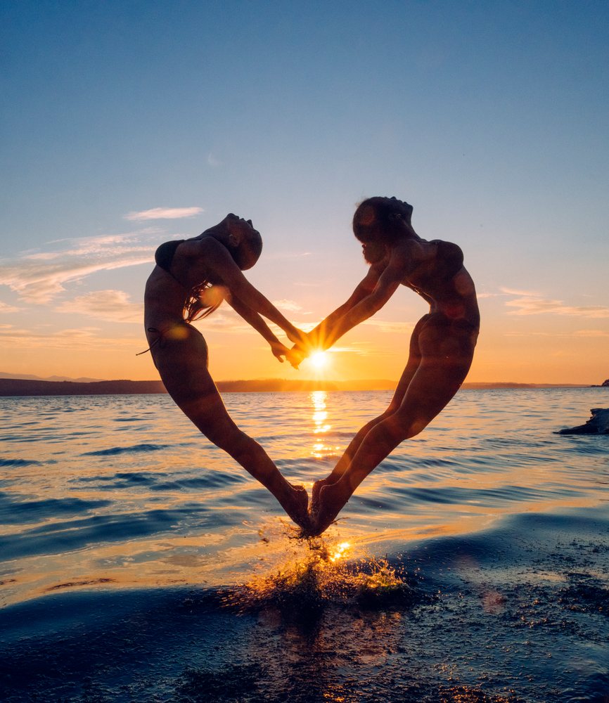 Two women practice partner acrobatics yoga at sunset by the water