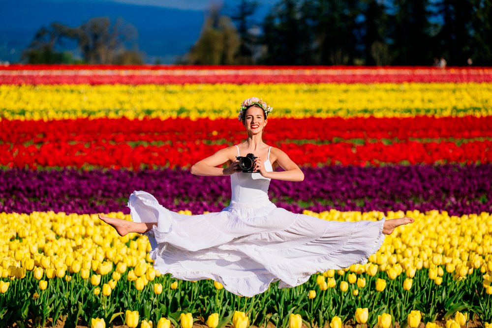 Ballet white dancer leaping with camera in colorful flower field