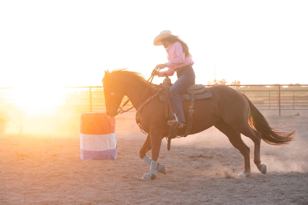 Cowgirl riding horse in dusty arena at sunset in Southwest USA