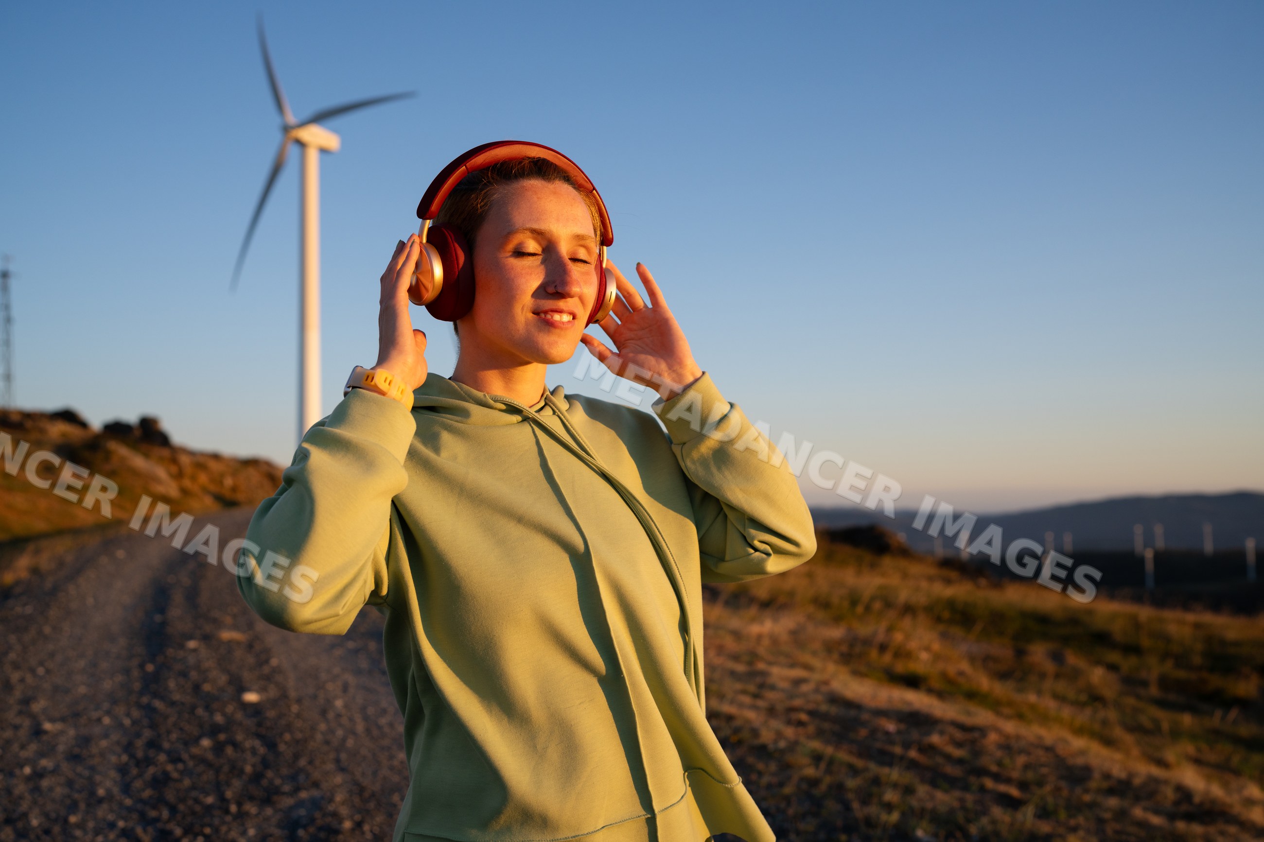 White Woman enjoying music outdoors near a wind turbine at sunset