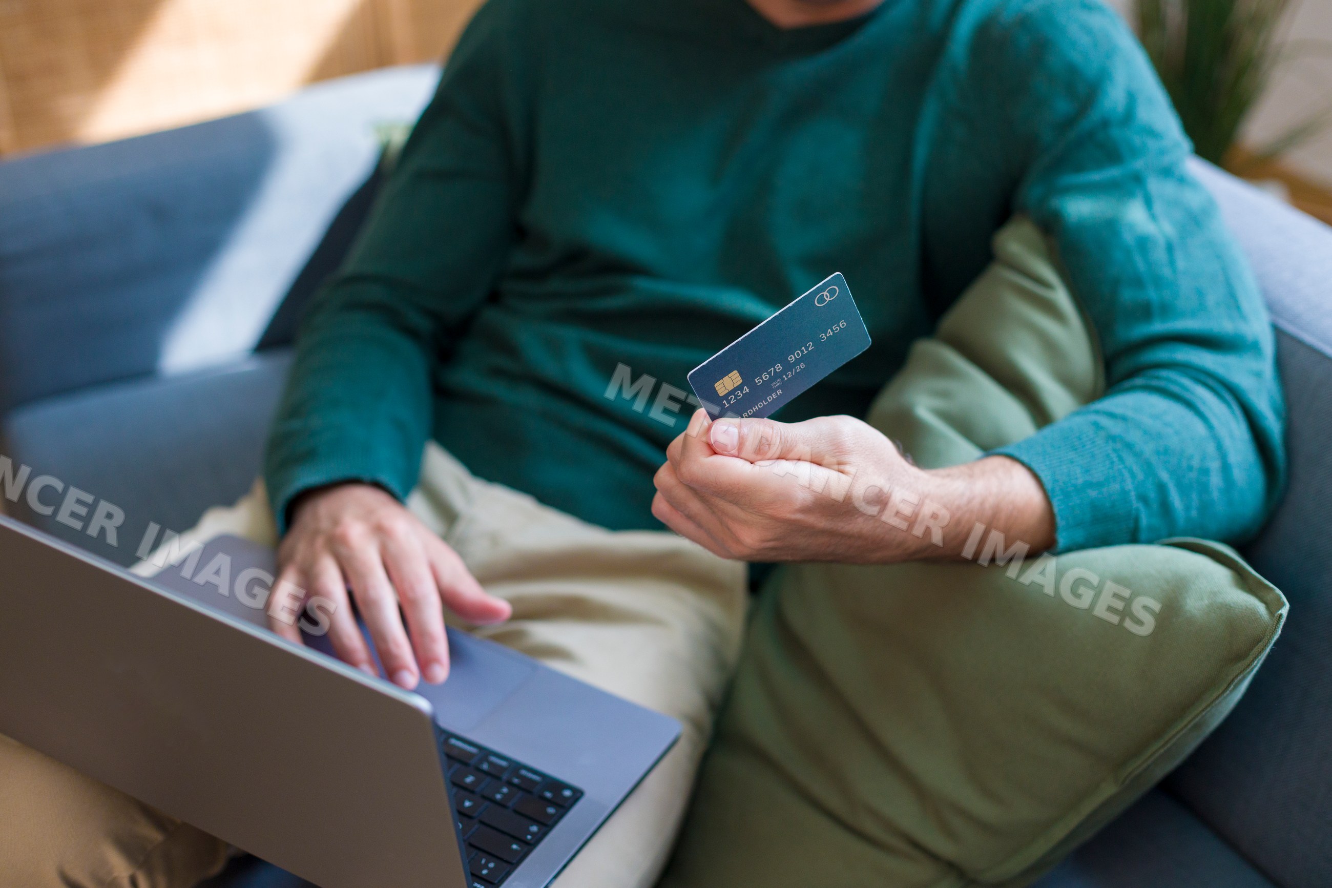 White person credit card using laptop on sofa at home