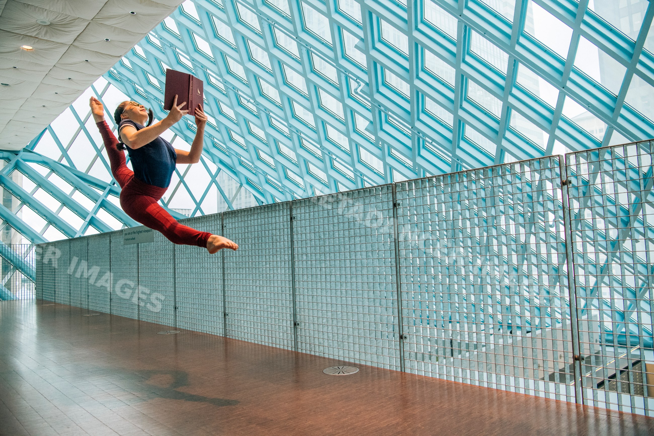 A woman jumps in a split leap holding a book in a library