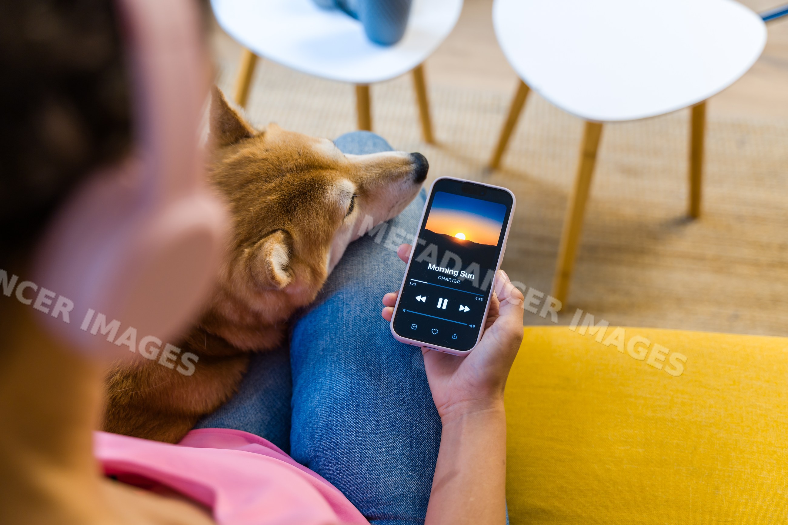 A Hispanic person listens to music on a smartphone with a dog resting