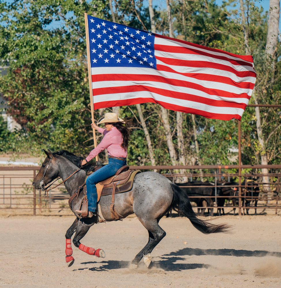 White woman riding horse holding american flag at Southwest USA ranch