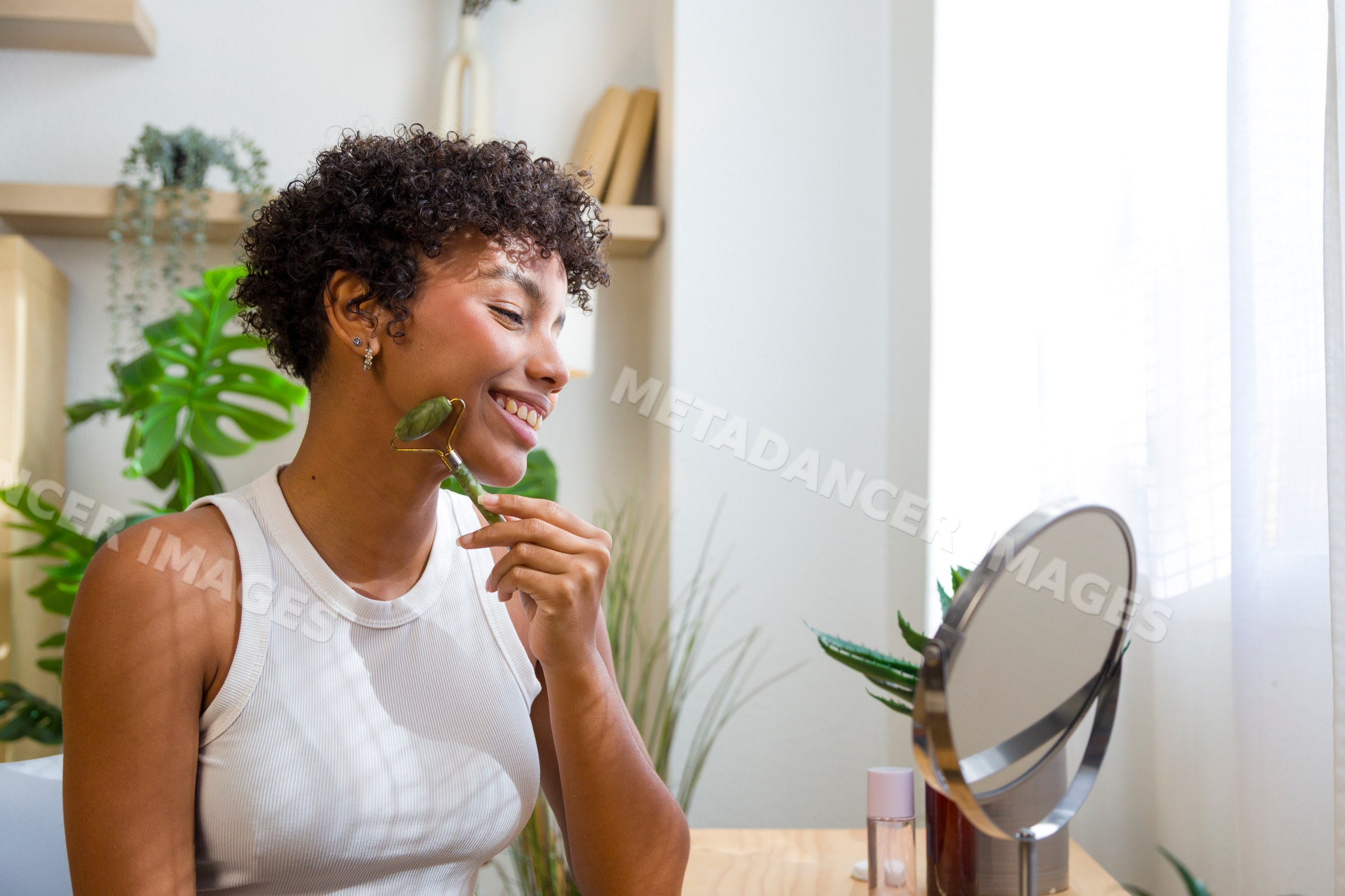 Young African American woman using facial roller looking in mirror