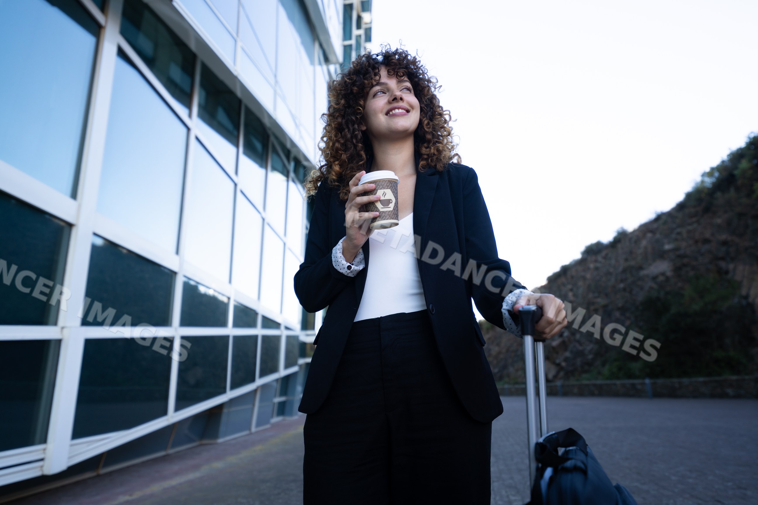 Businesswoman holding coffee and suitcase outside glass building