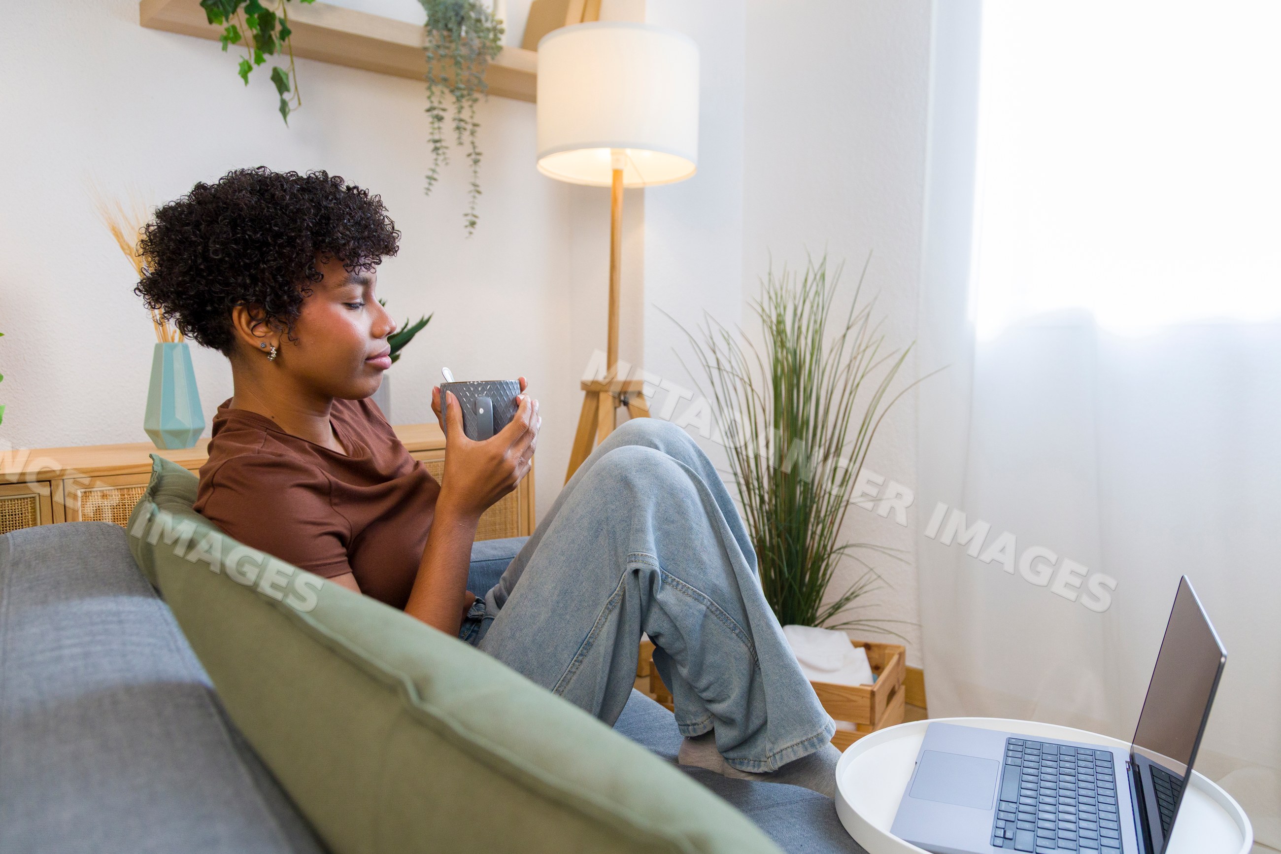 Young African American woman sitting on sofa drinking from cup