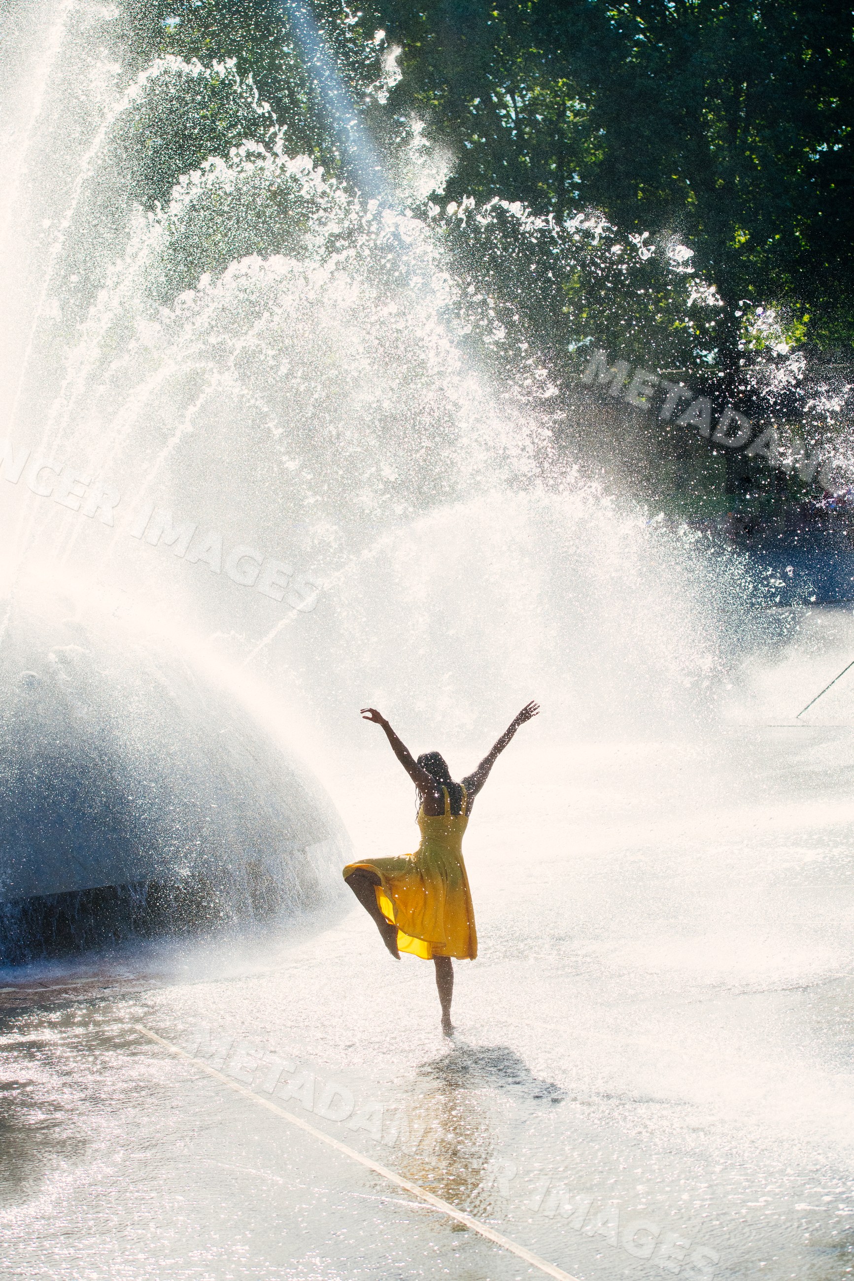 South Asian woman dancing in water spray of large outdoor fountain