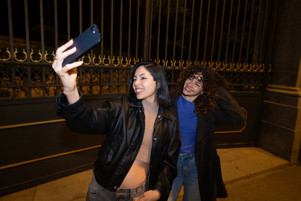 Two Hispanic and white women taking a selfie outdoors at night