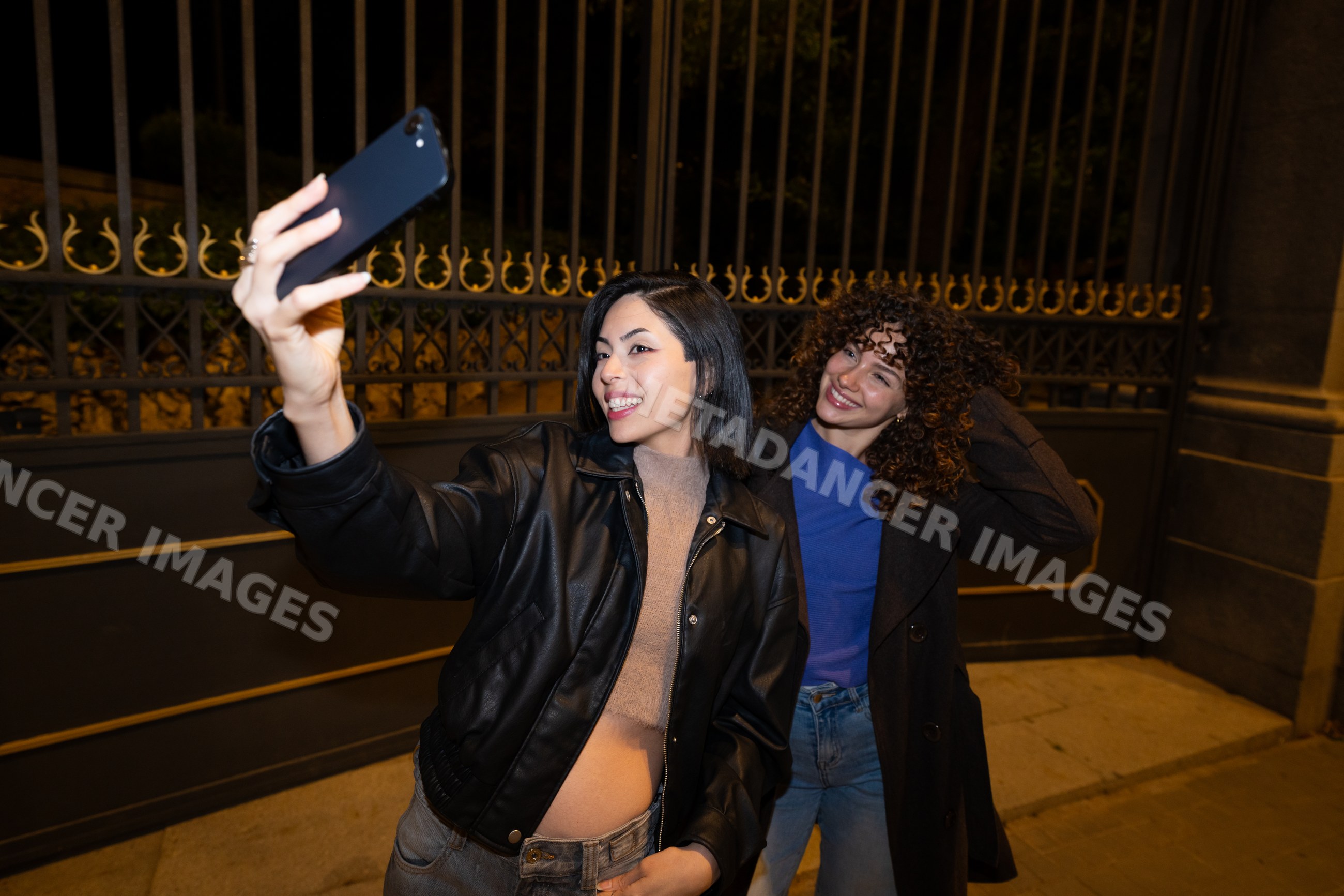 Two Hispanic and white women taking a selfie outdoors at night
