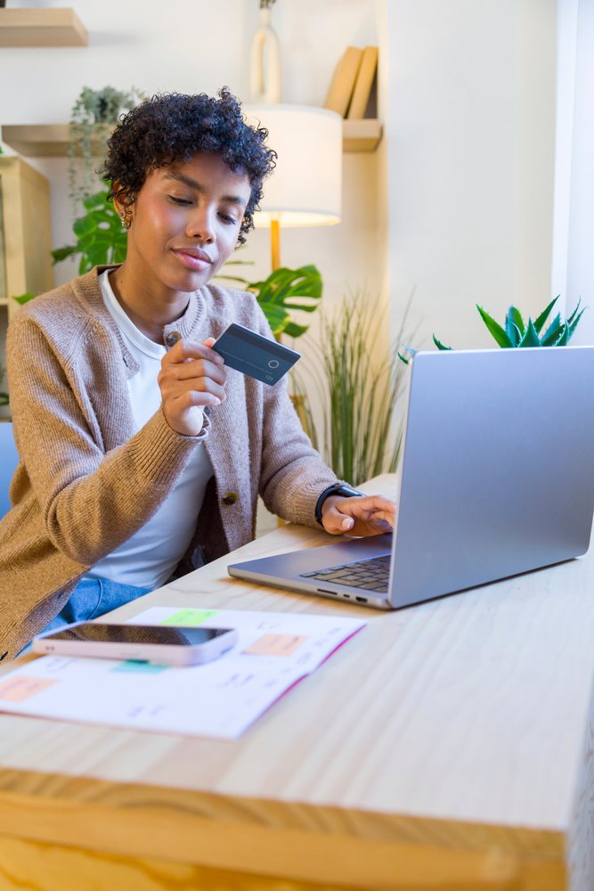 African American woman holding credit card using laptop in home office