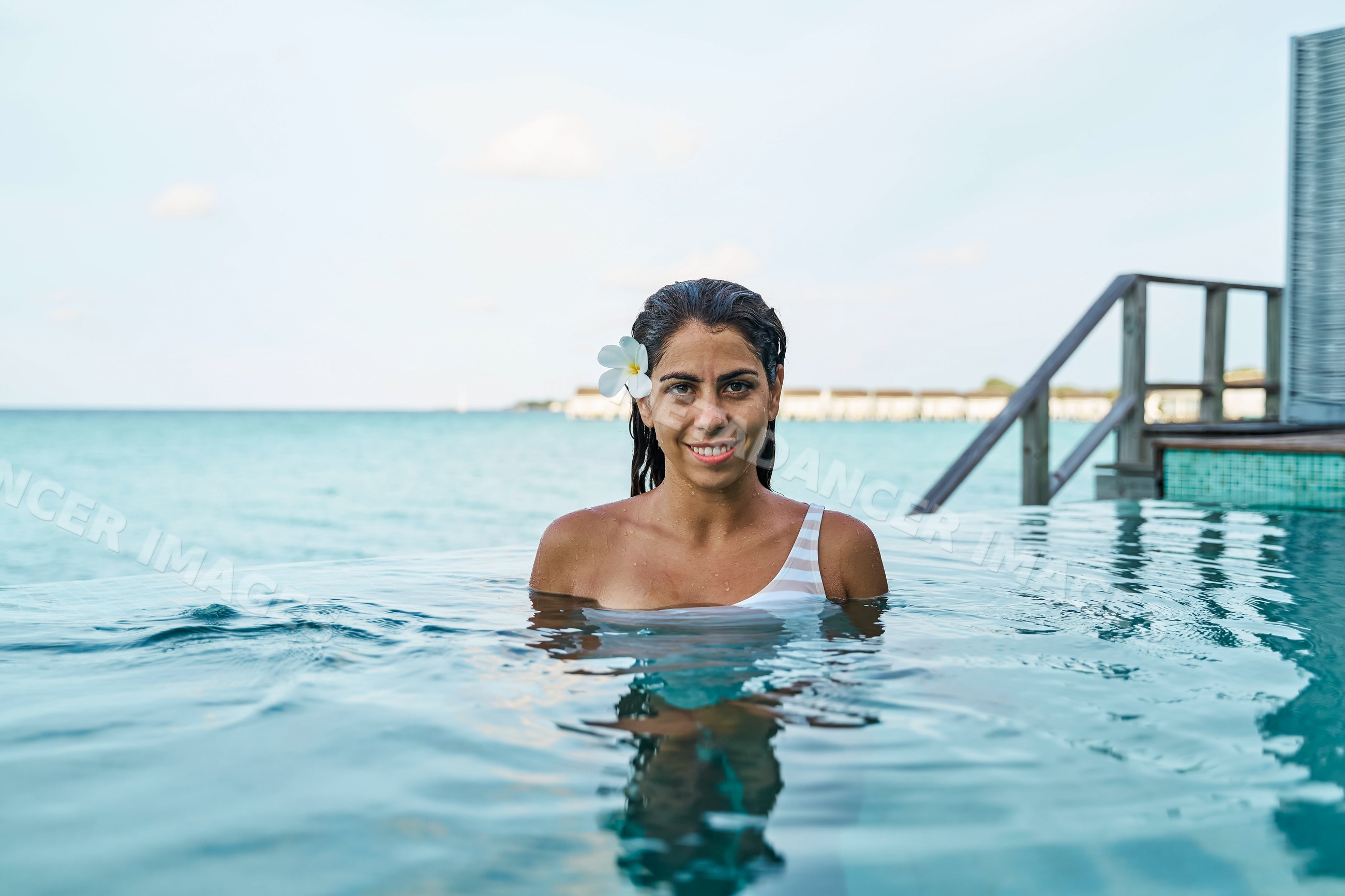 A smiling white woman enjoys an infinity pool with ocean view