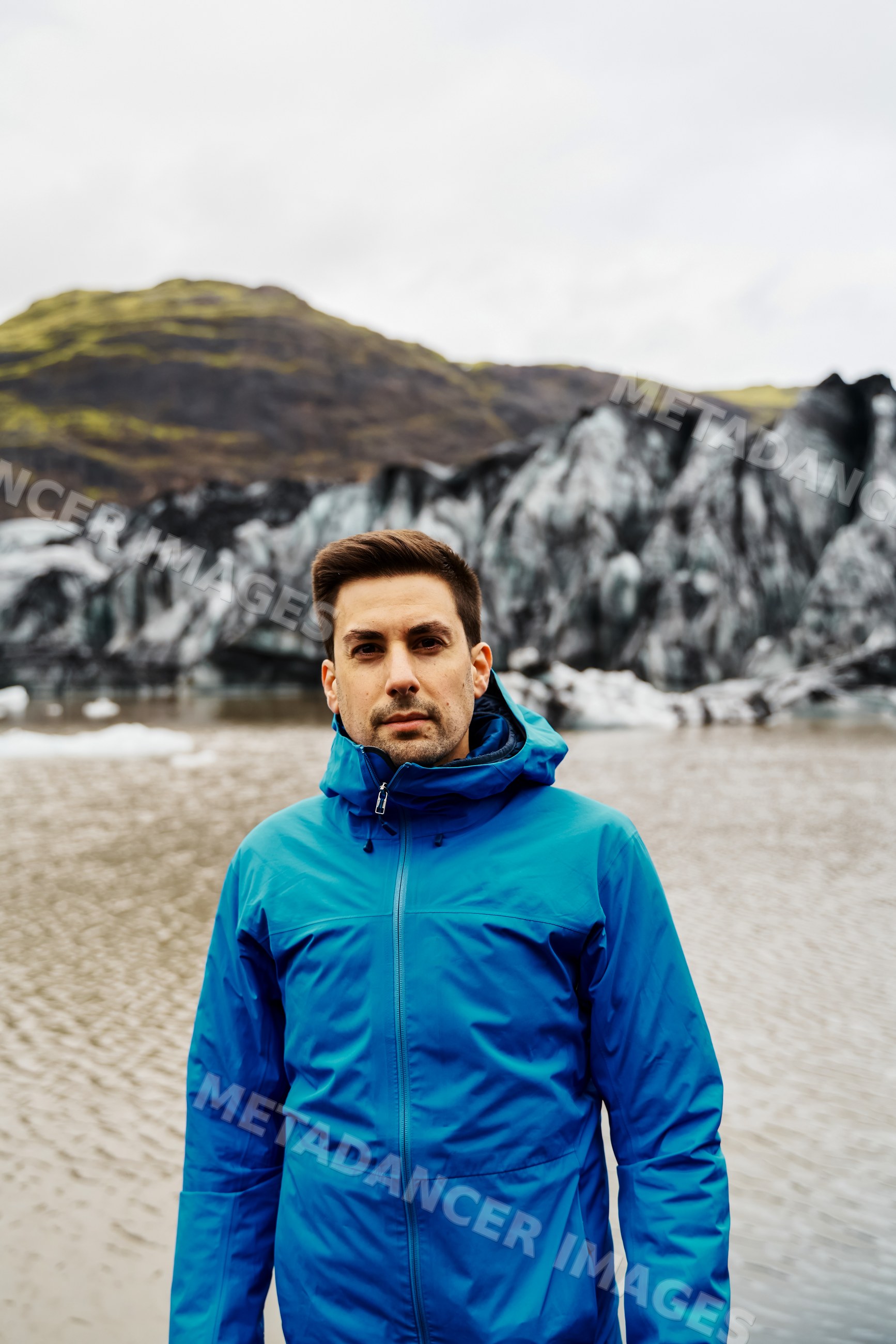 A white man stands outdoors near a glacier and lake