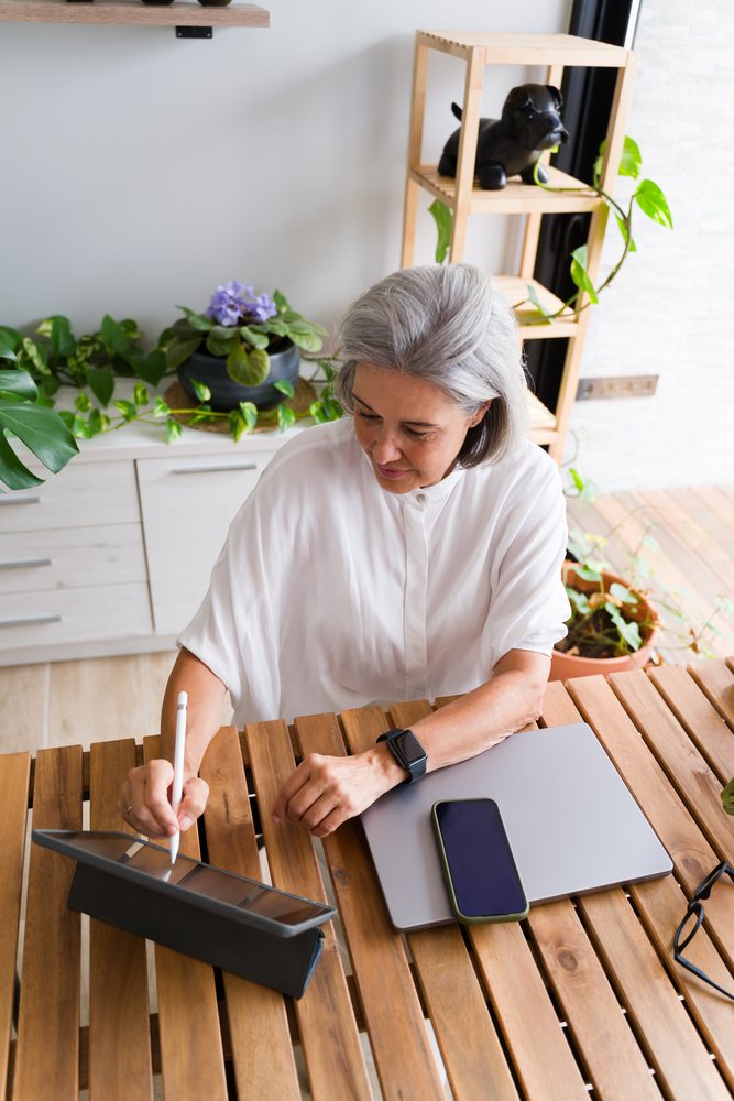 White Woman using digital pen on tablet at wooden table in home office