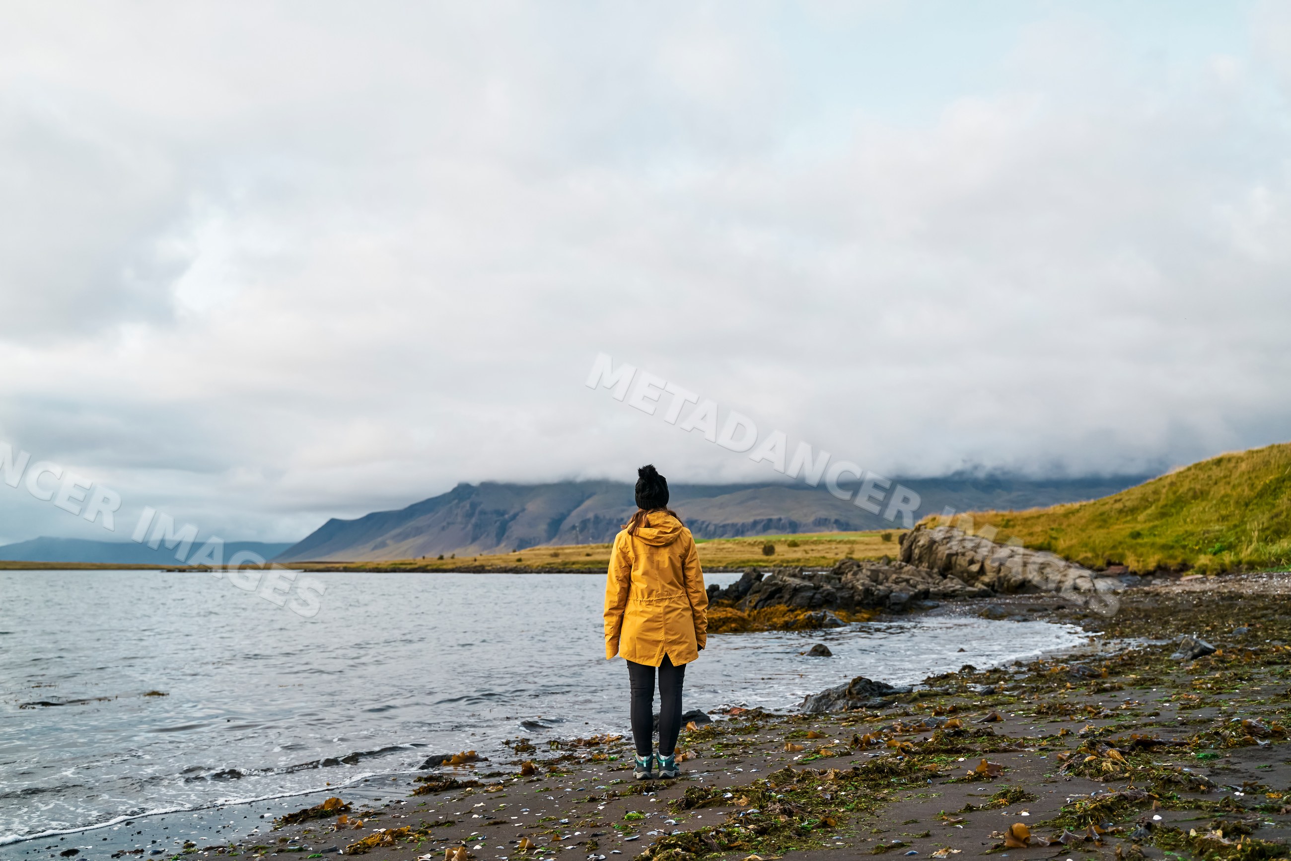 A white woman stands on a rocky shore looking