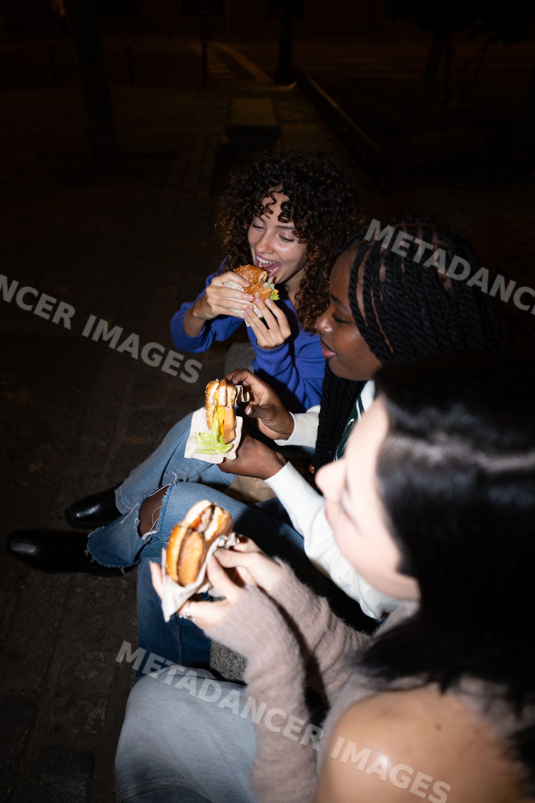 Three Hispanic, white and Black people eating burgers on a bench