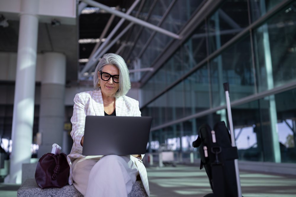 Businesswoman working on laptop outside modern airport terminal