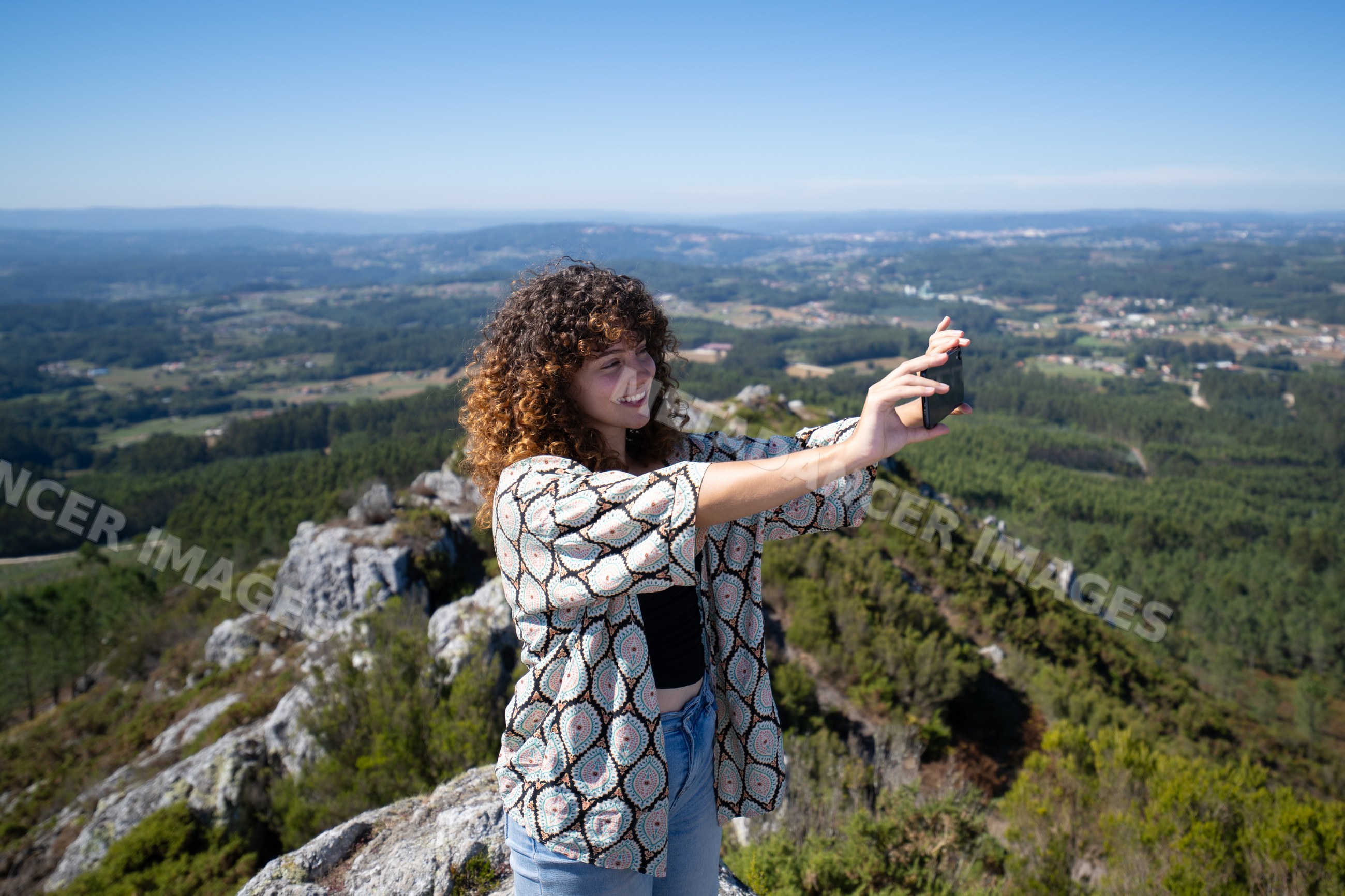 White woman taking selfie on mountain peak with valley view