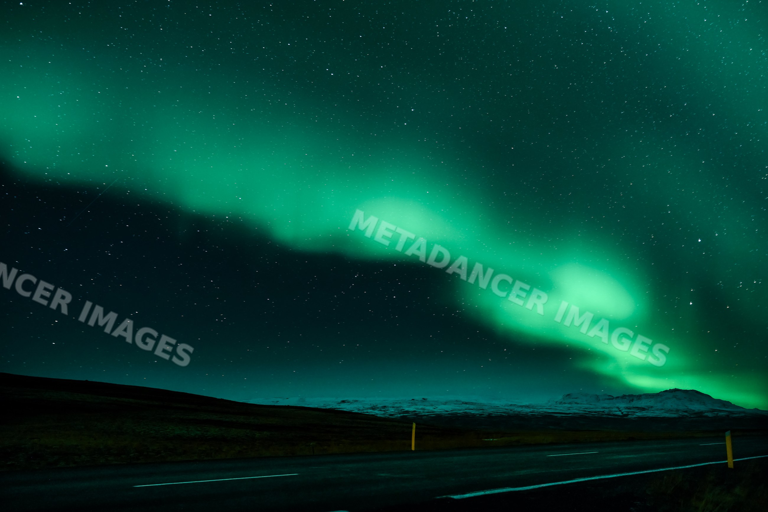 Green aurora borealis lights illuminate a mountain road