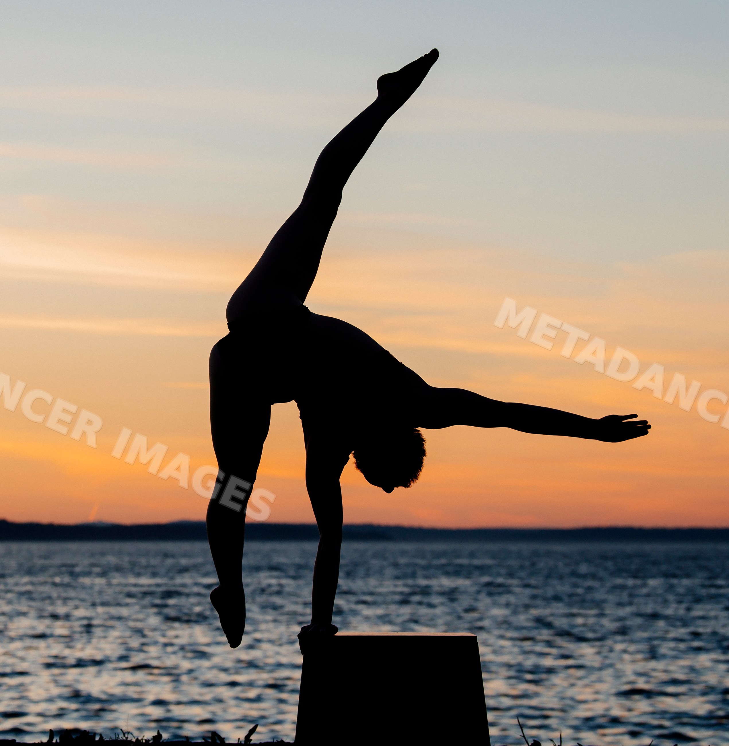 Silhouette of white person doing handstand by lake at sunset