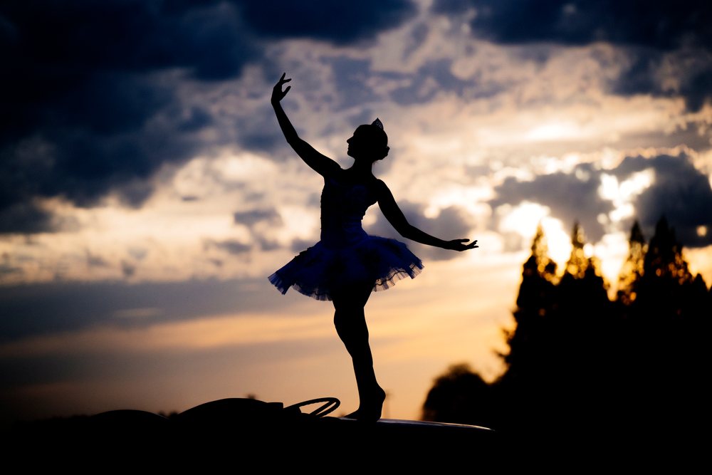 Ballet white dancer silhouette posing gracefully outdoors at sunset