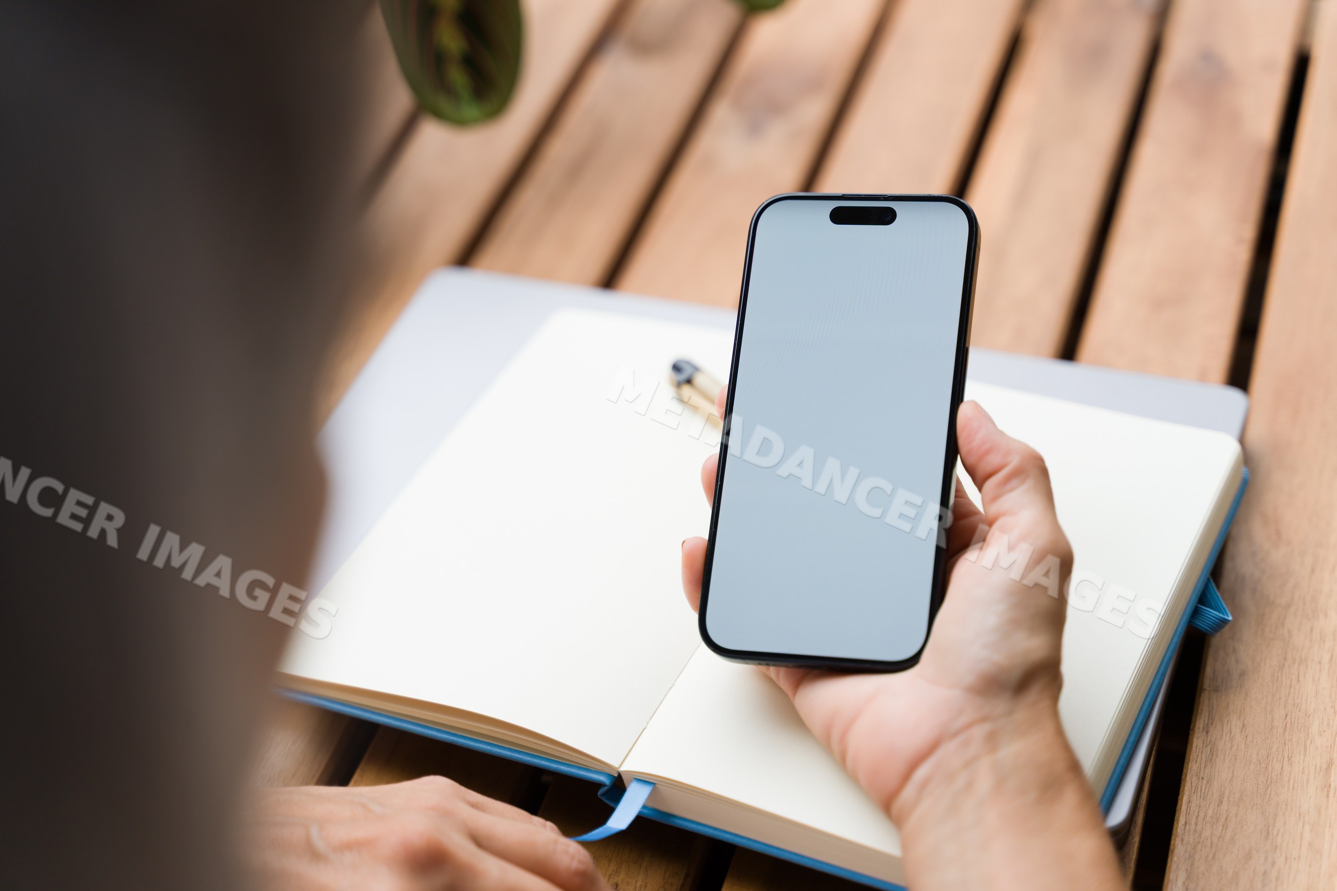 Hand holding smartphone with blank screen over open notebook on wooden
