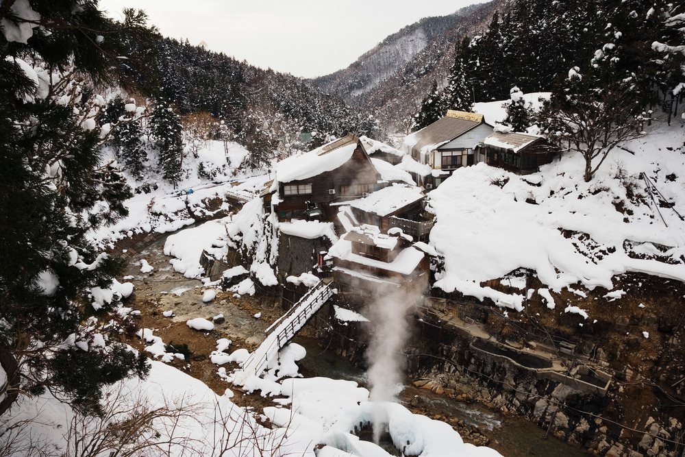Jigokudani onsen hot spring with snow-covered river and wooden houses