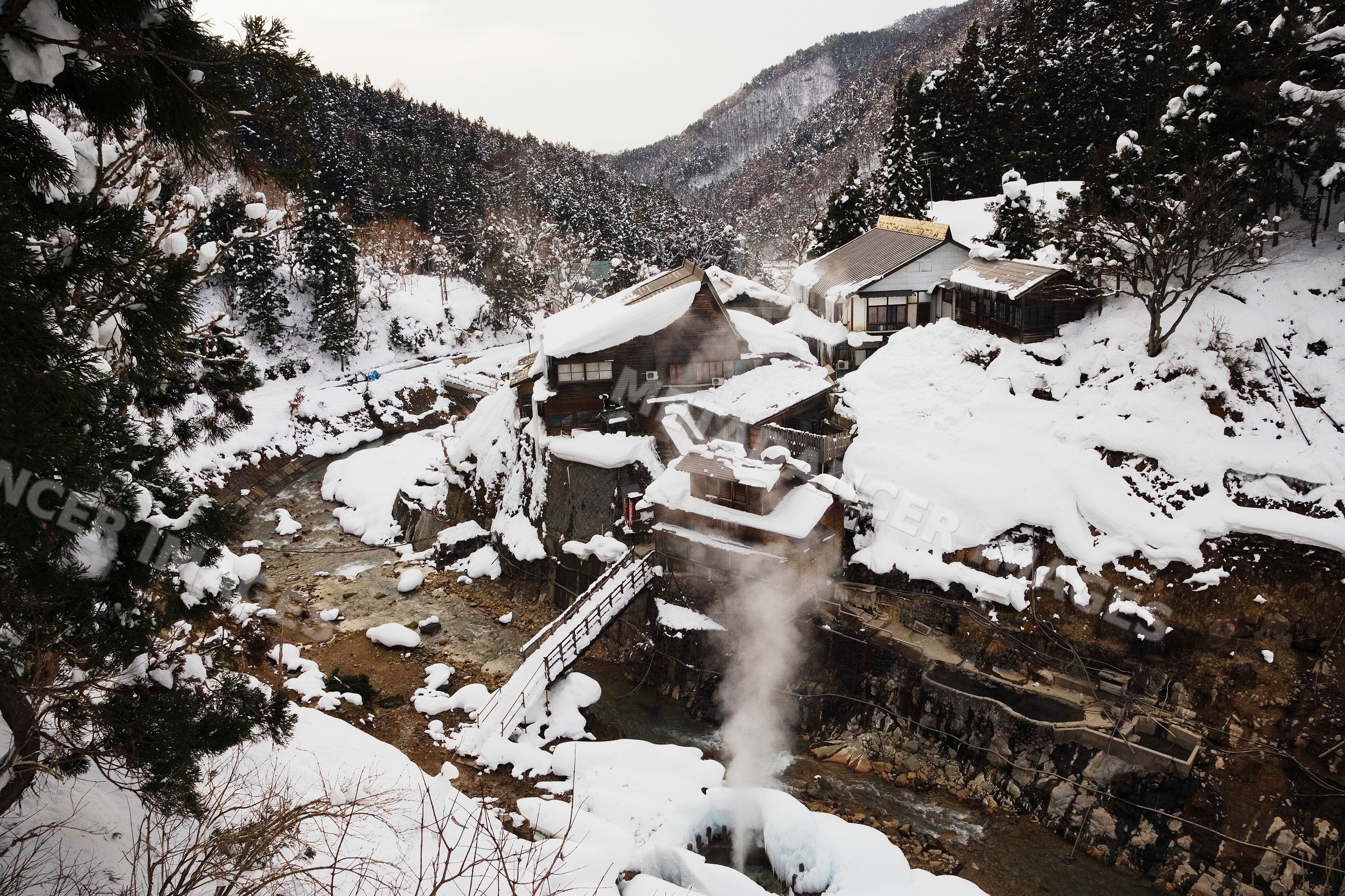Jigokudani onsen hot spring with snow-covered river and wooden houses