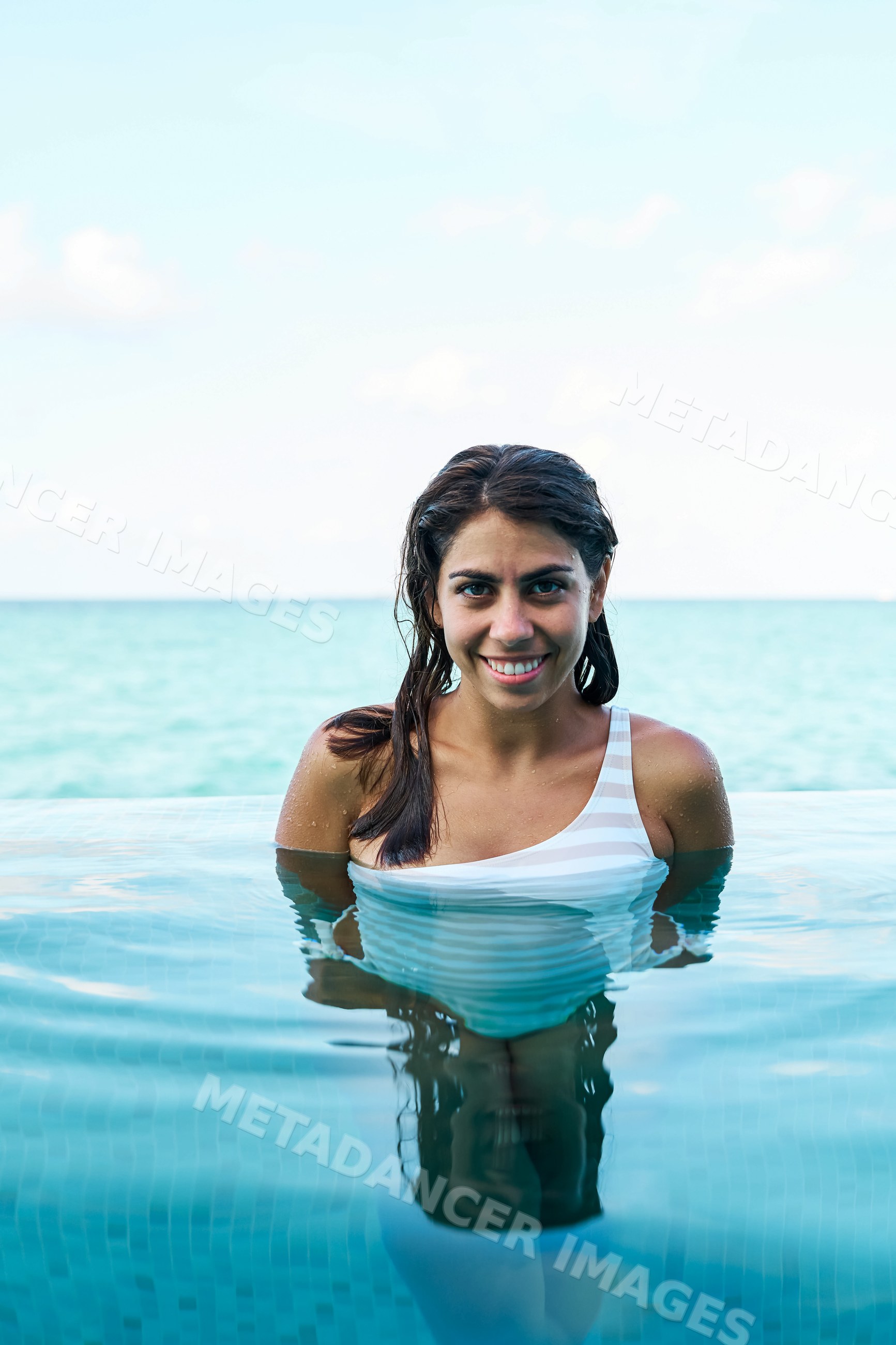A woman in a white swimsuit enjoys an infinity pool with sea view