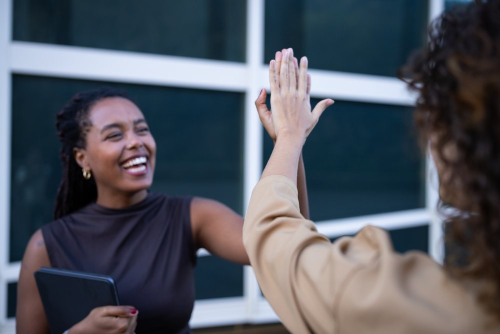 Two African American and white women exchanging a high five outside