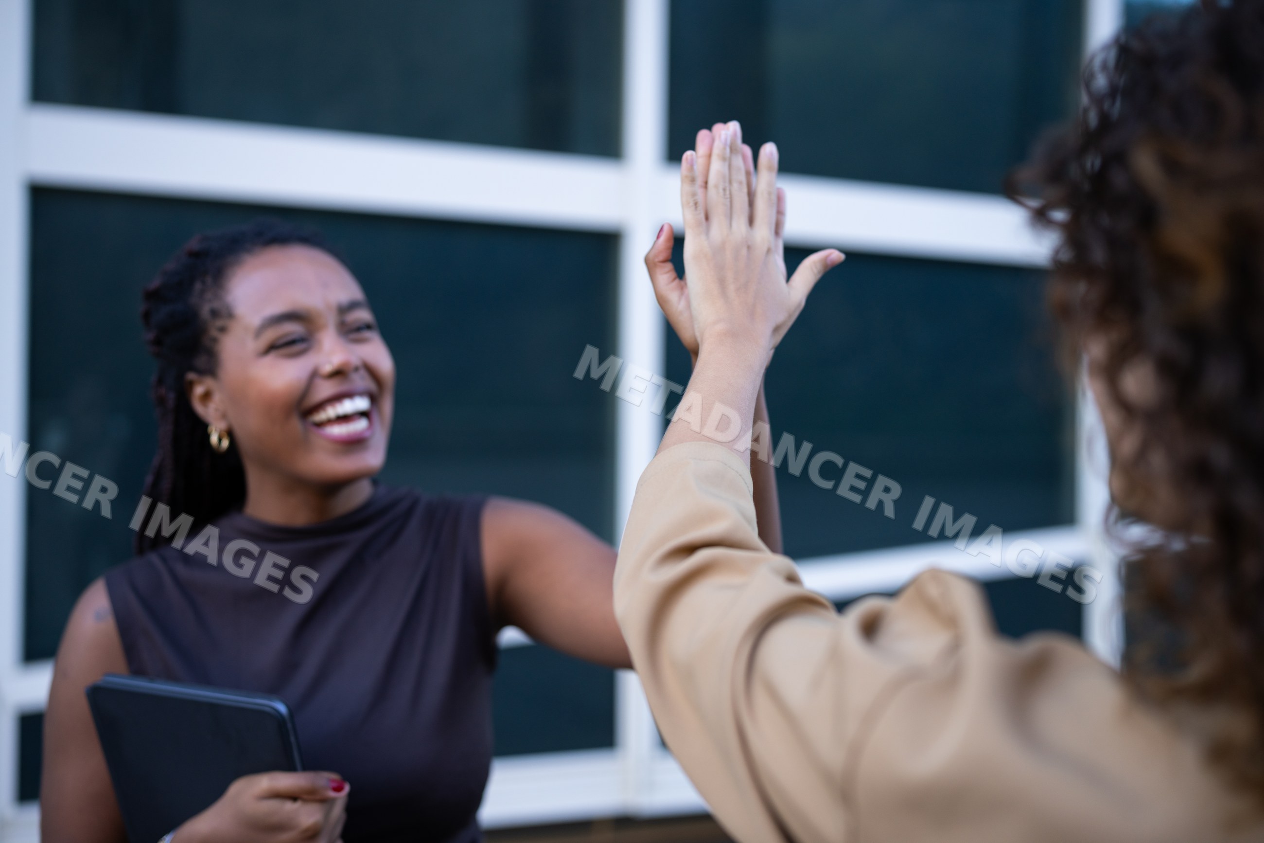 Two African American and white women exchanging a high five outside