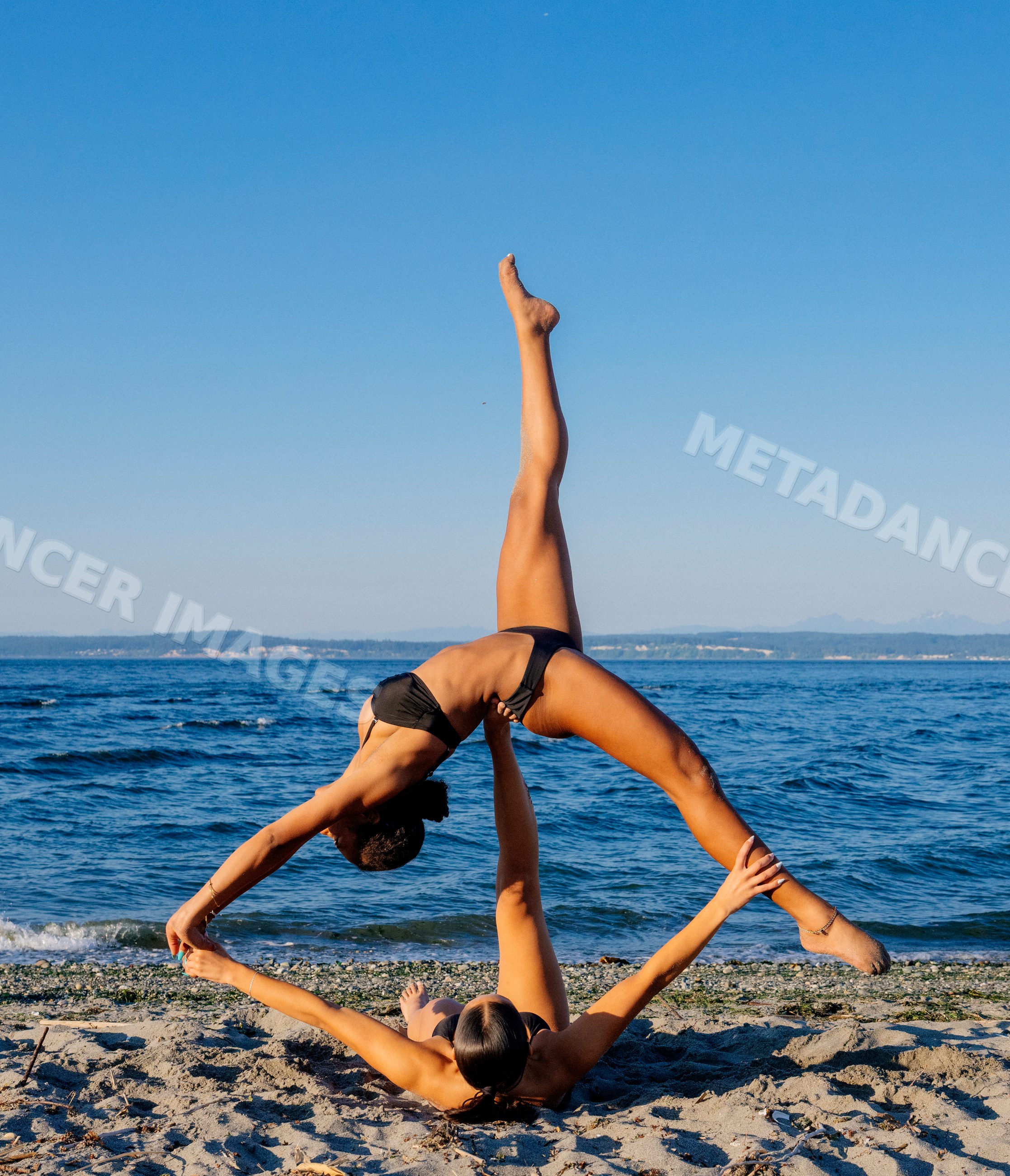 Two women doing partner acrobatics yoga on a beach in wa USA