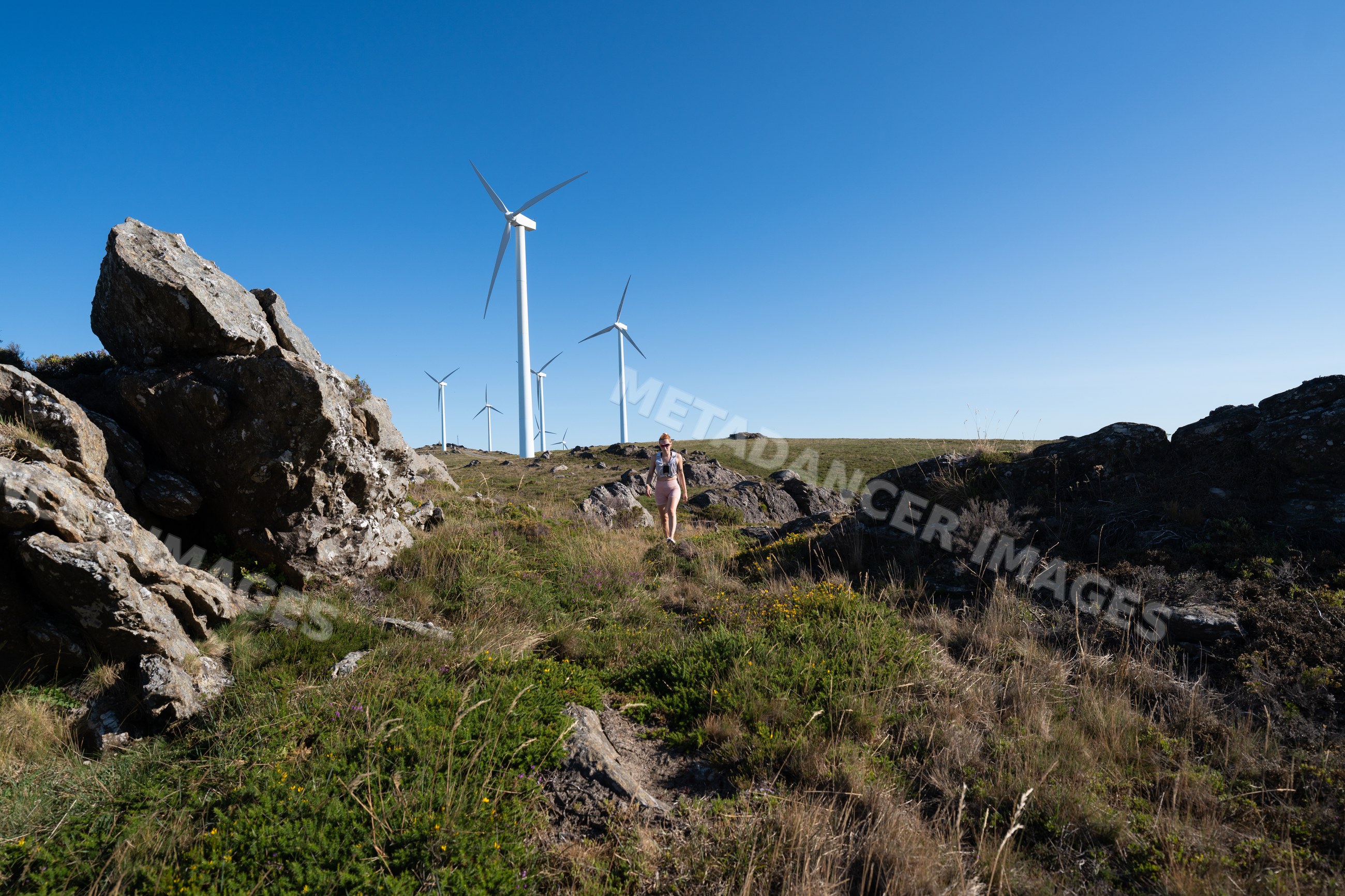 A white woman hiking near wind turbines in a rocky landscape
