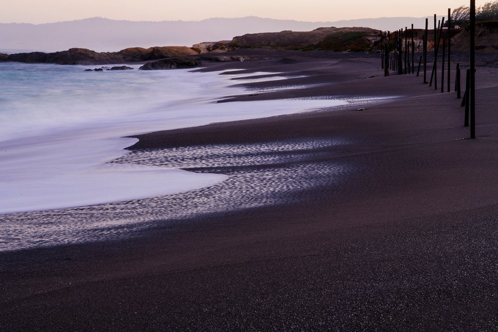 Black sand beach with waves and wooden poles along northern California