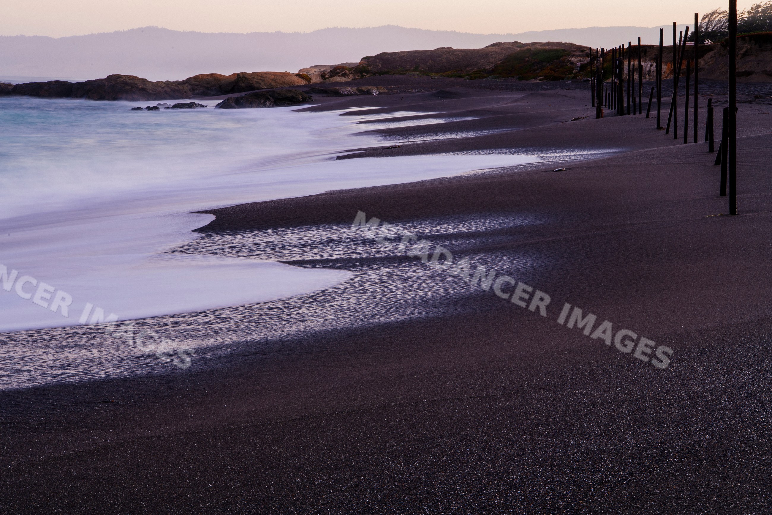 Black sand beach with waves and wooden poles along northern California