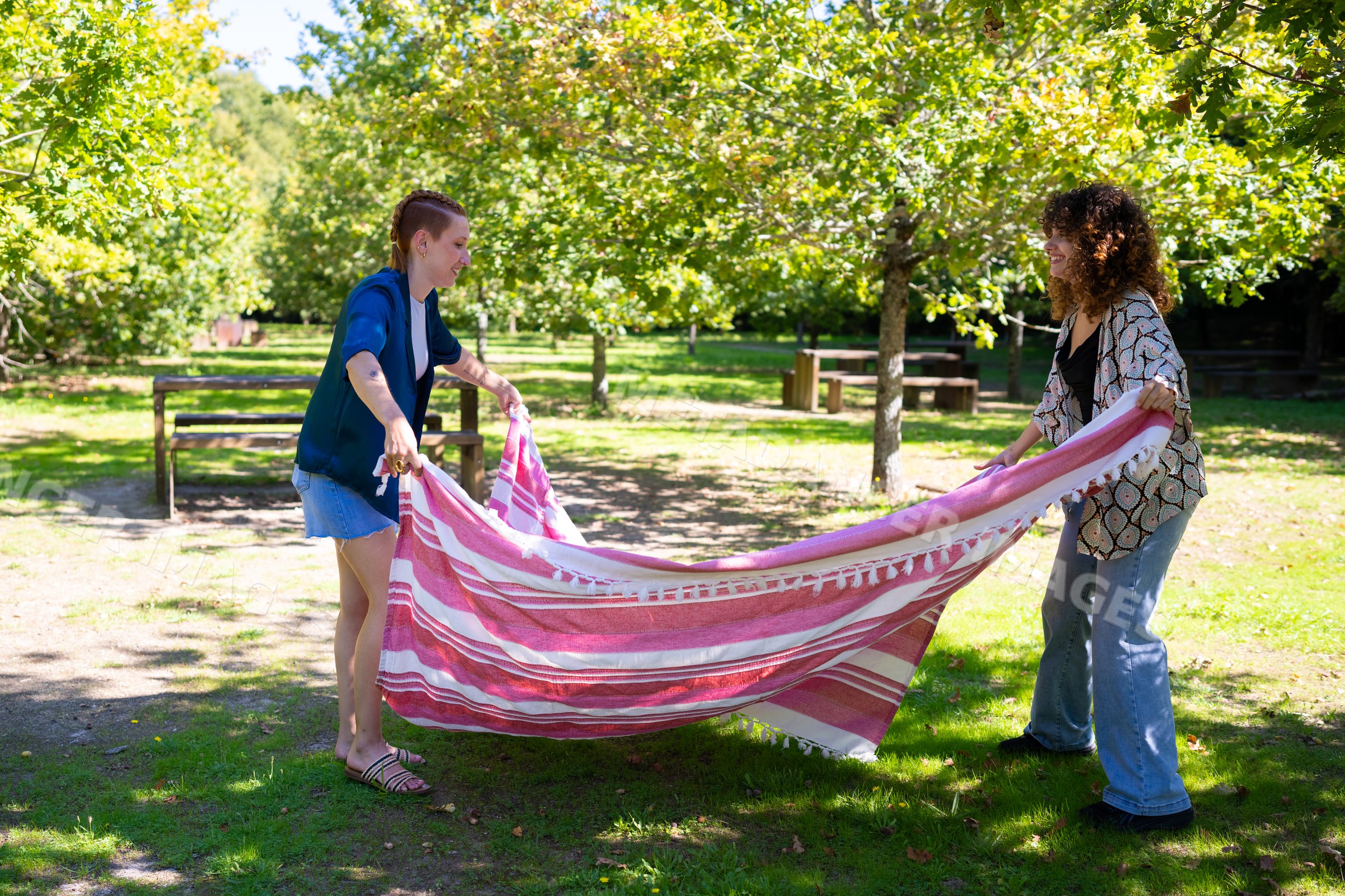 Two white women spreading picnic blanket in sunny green park