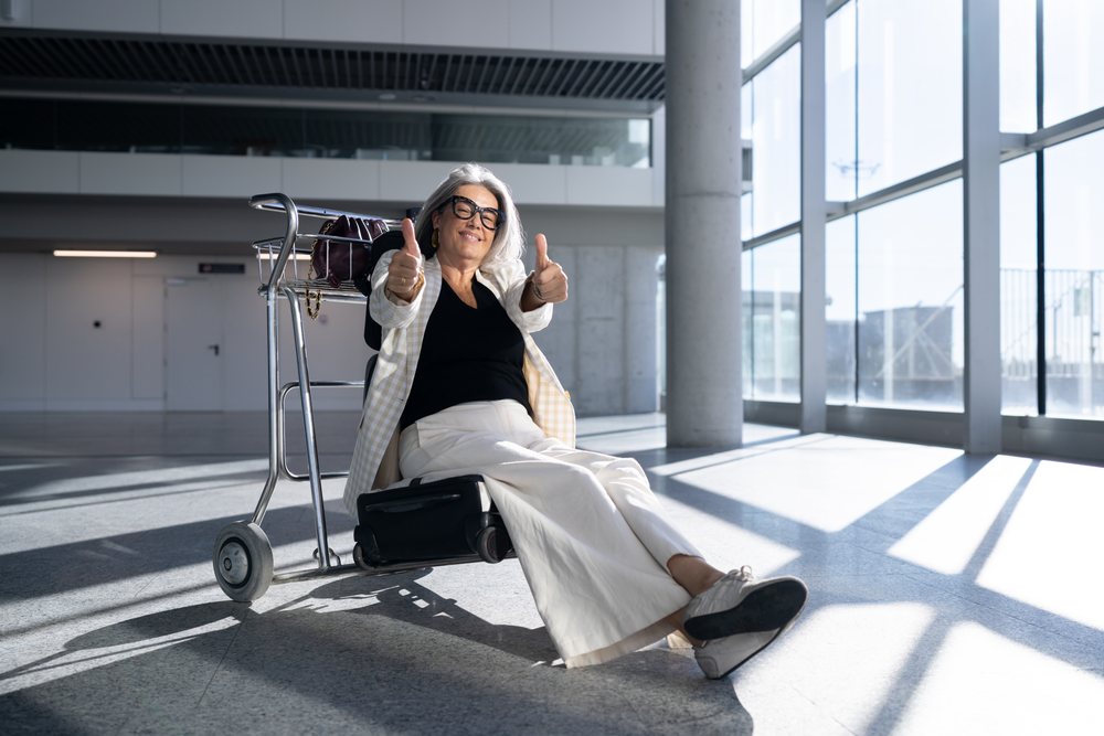 White woman traveler showing thumbs up sitting on luggage trolley