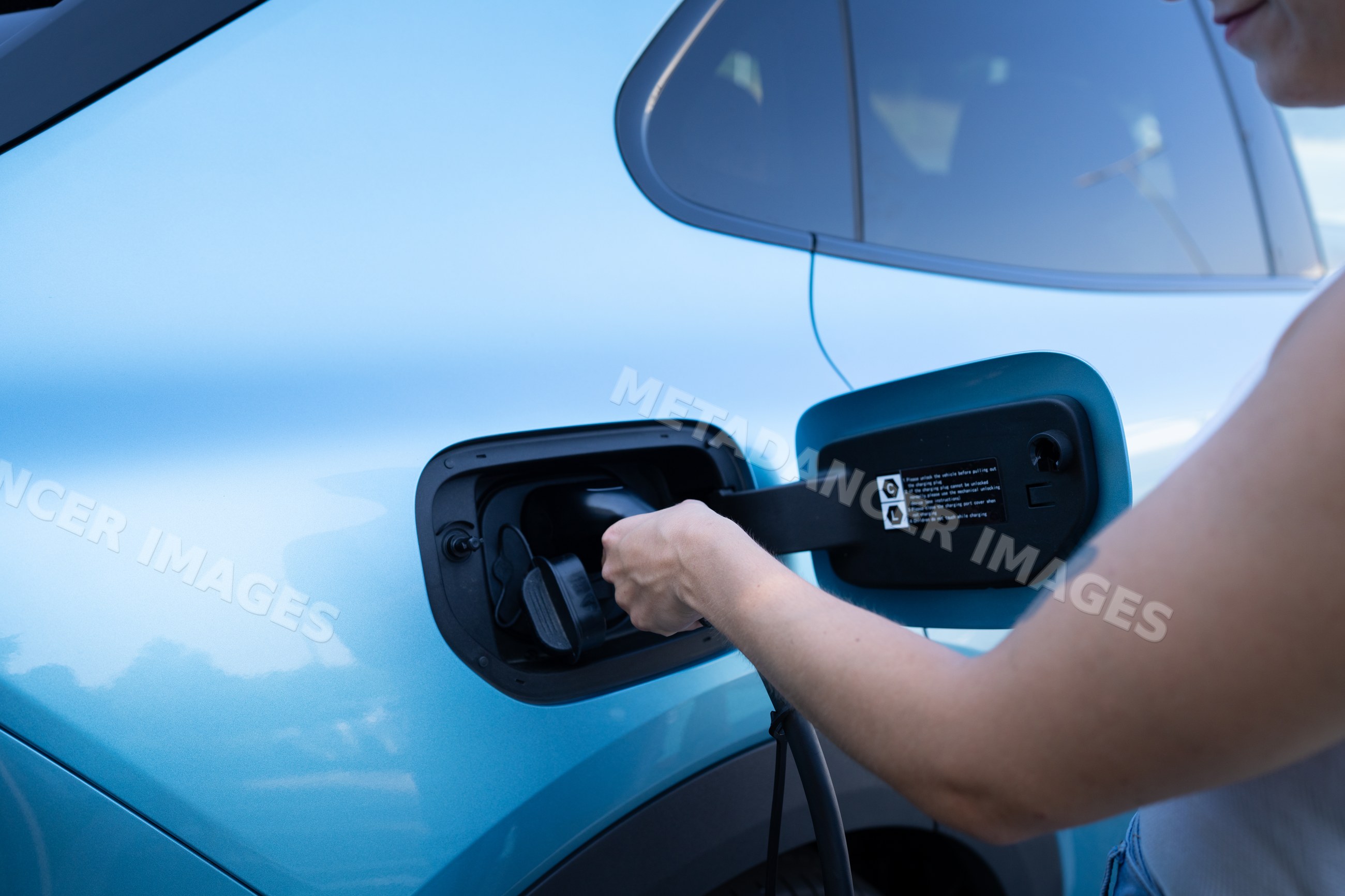 A white person charges a blue electric vehicle showcasing sustainable