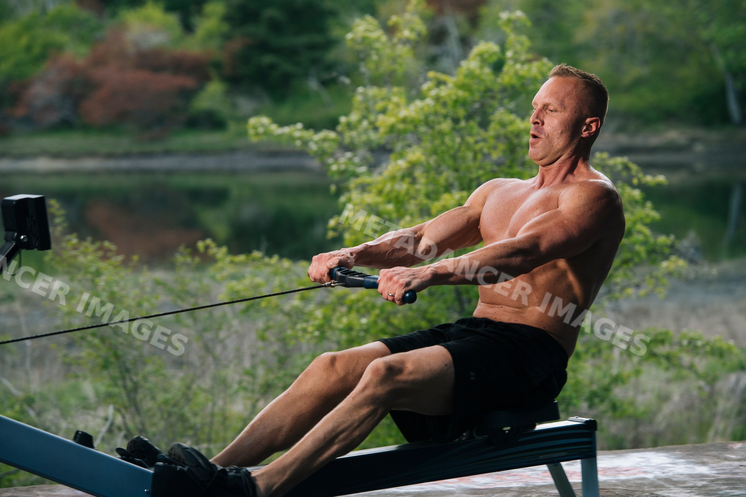 White man rowing on exercise machine outdoors by lake