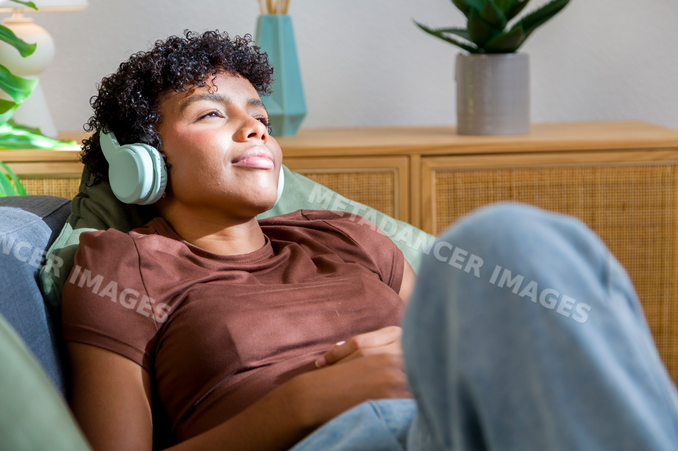 Young African American woman relaxing on sofa listening to headphones