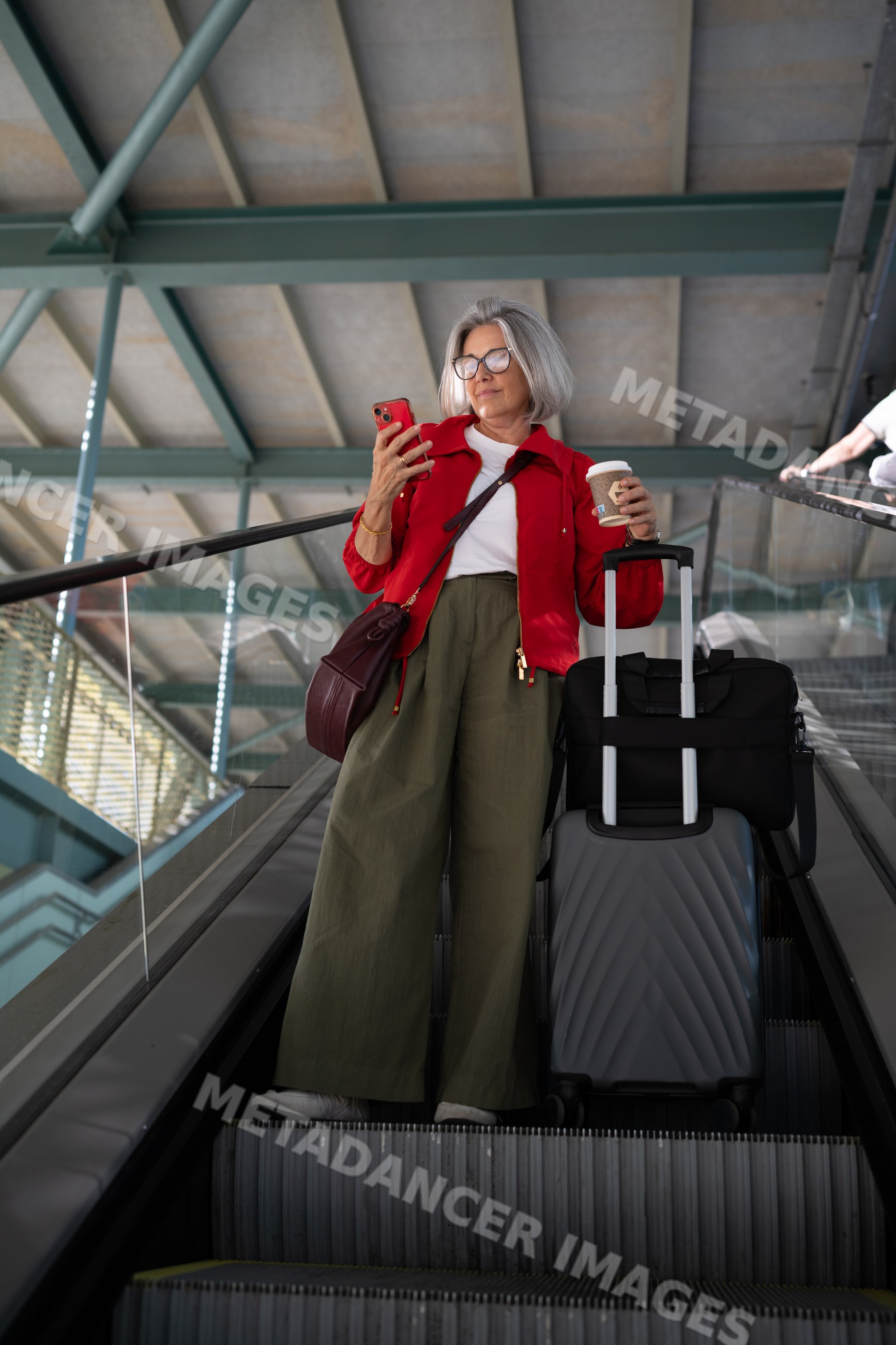 White woman standing on escalator with luggage and coffee