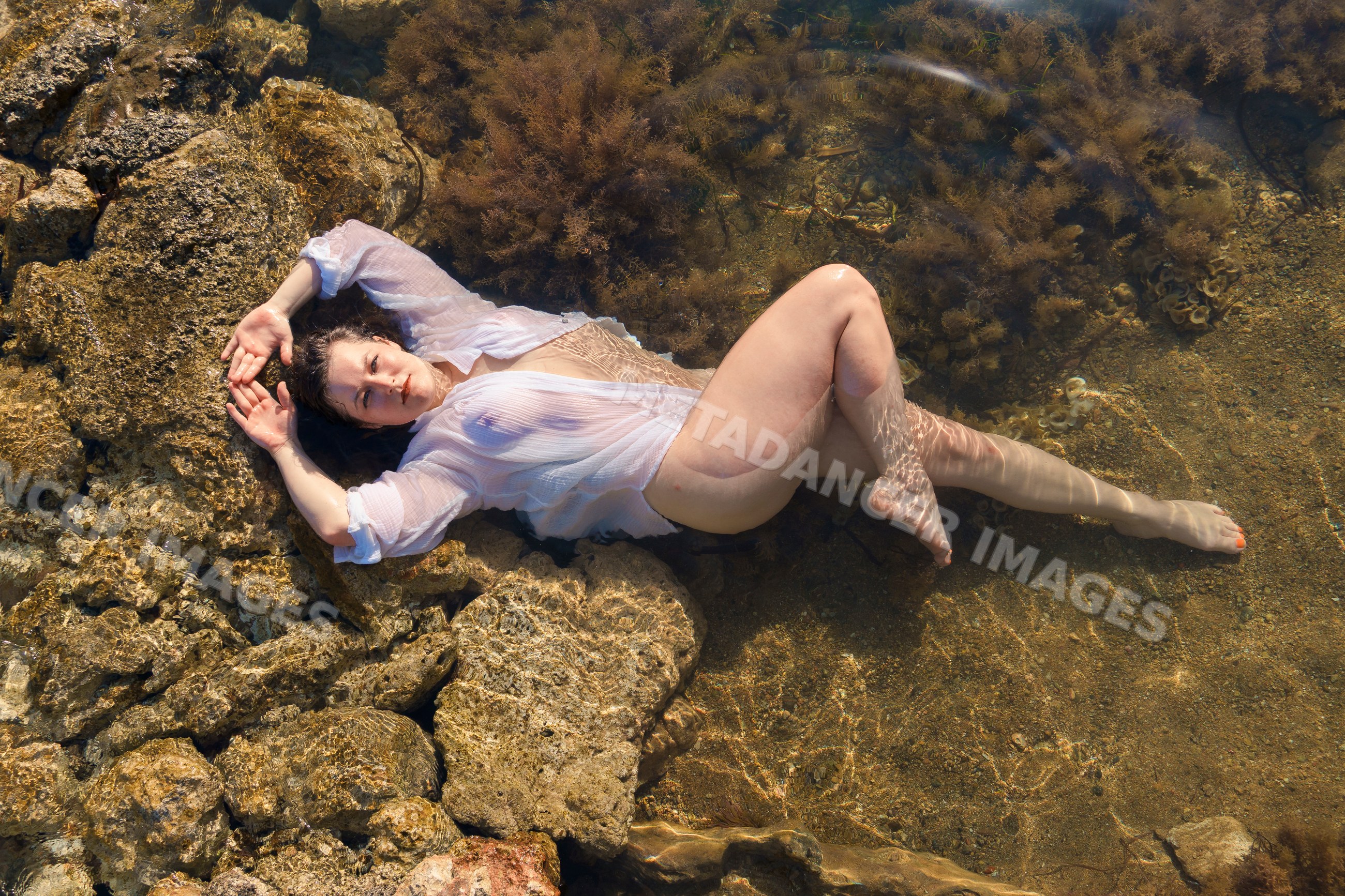 White woman lying in shallow water among rocks and seaweed in Ibiza