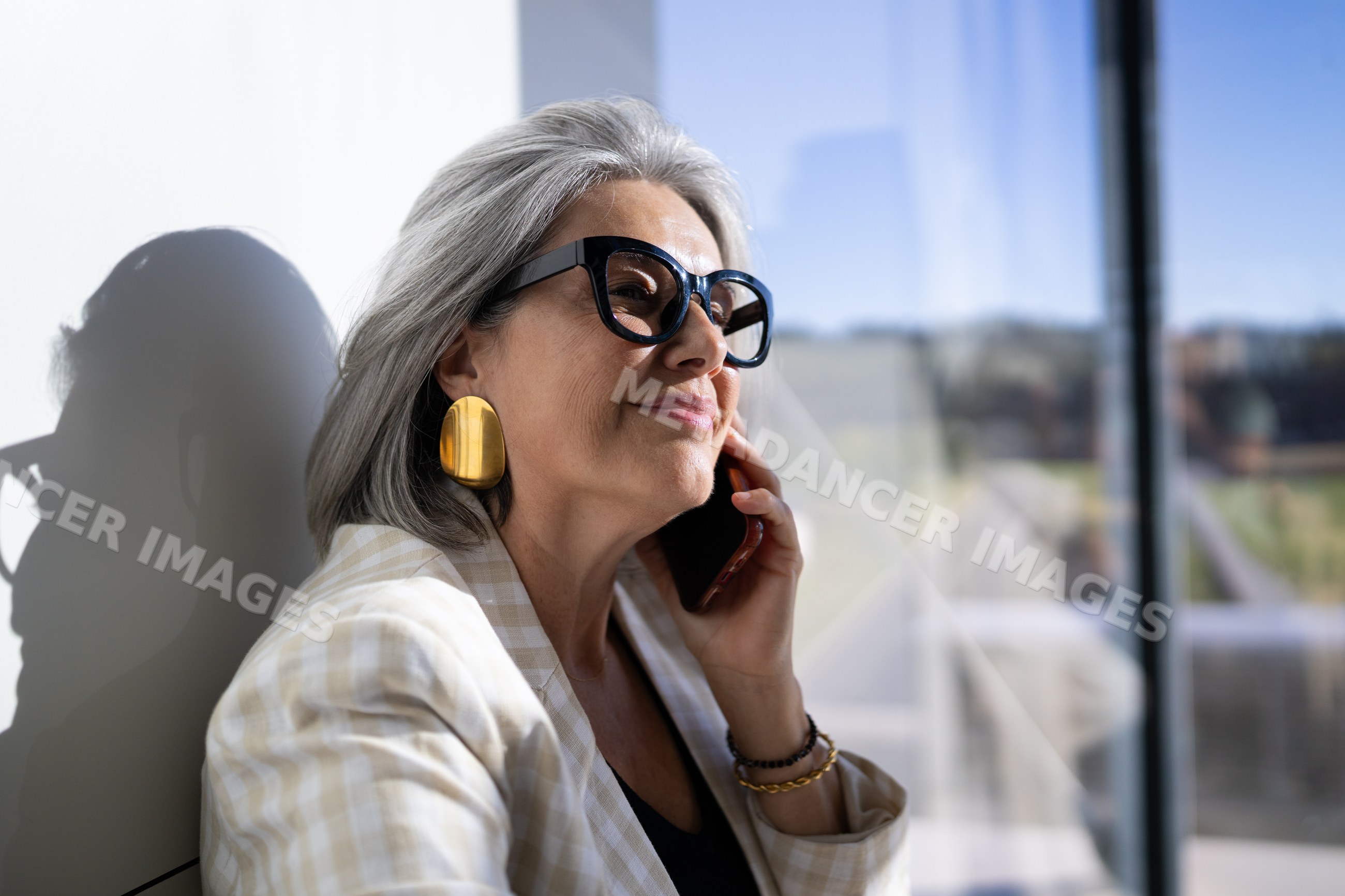 White woman with gray hair talking on the phone outside a modern