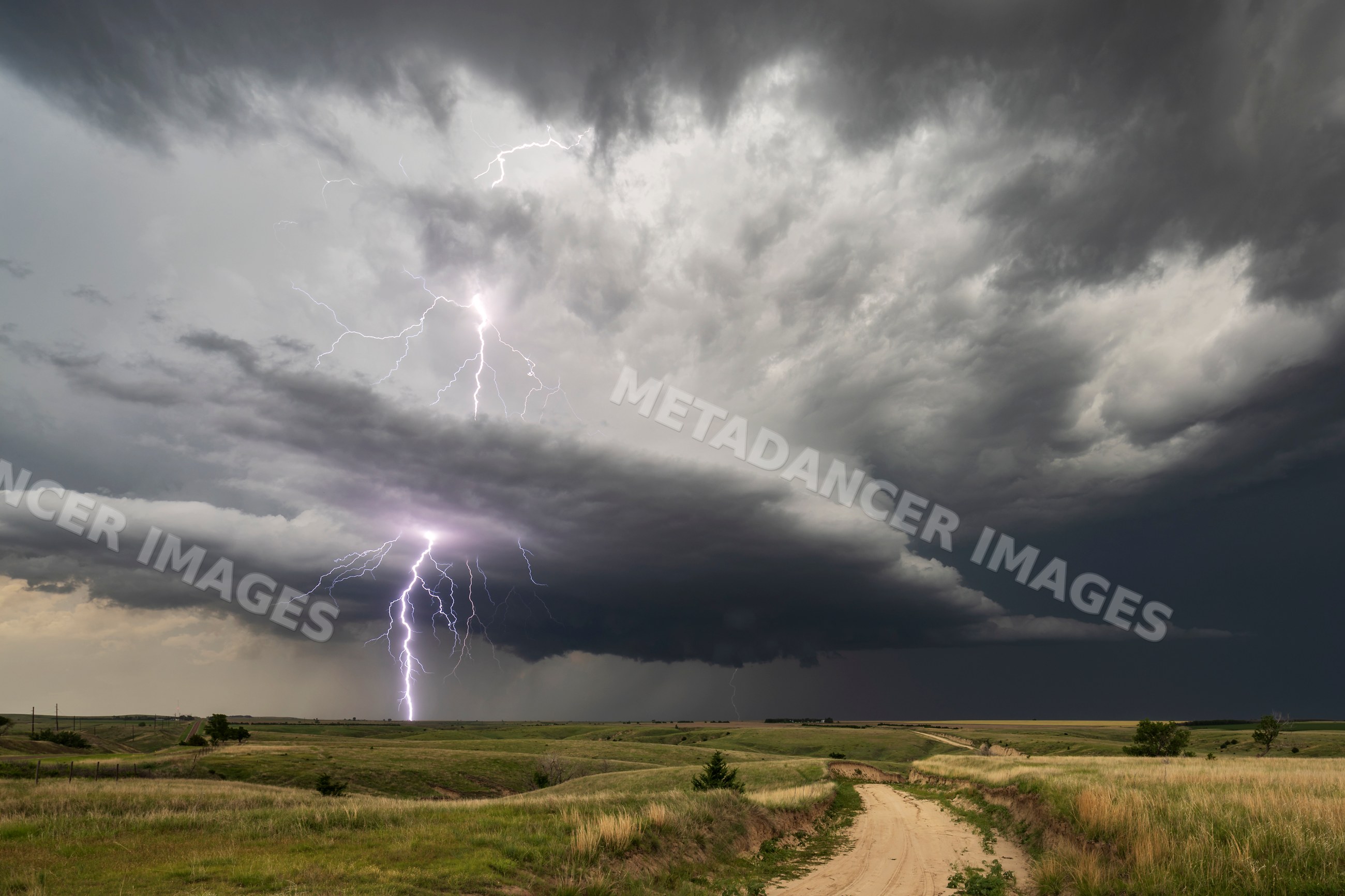 Lightning striking storm cloud over rural road in nebraska grasslands