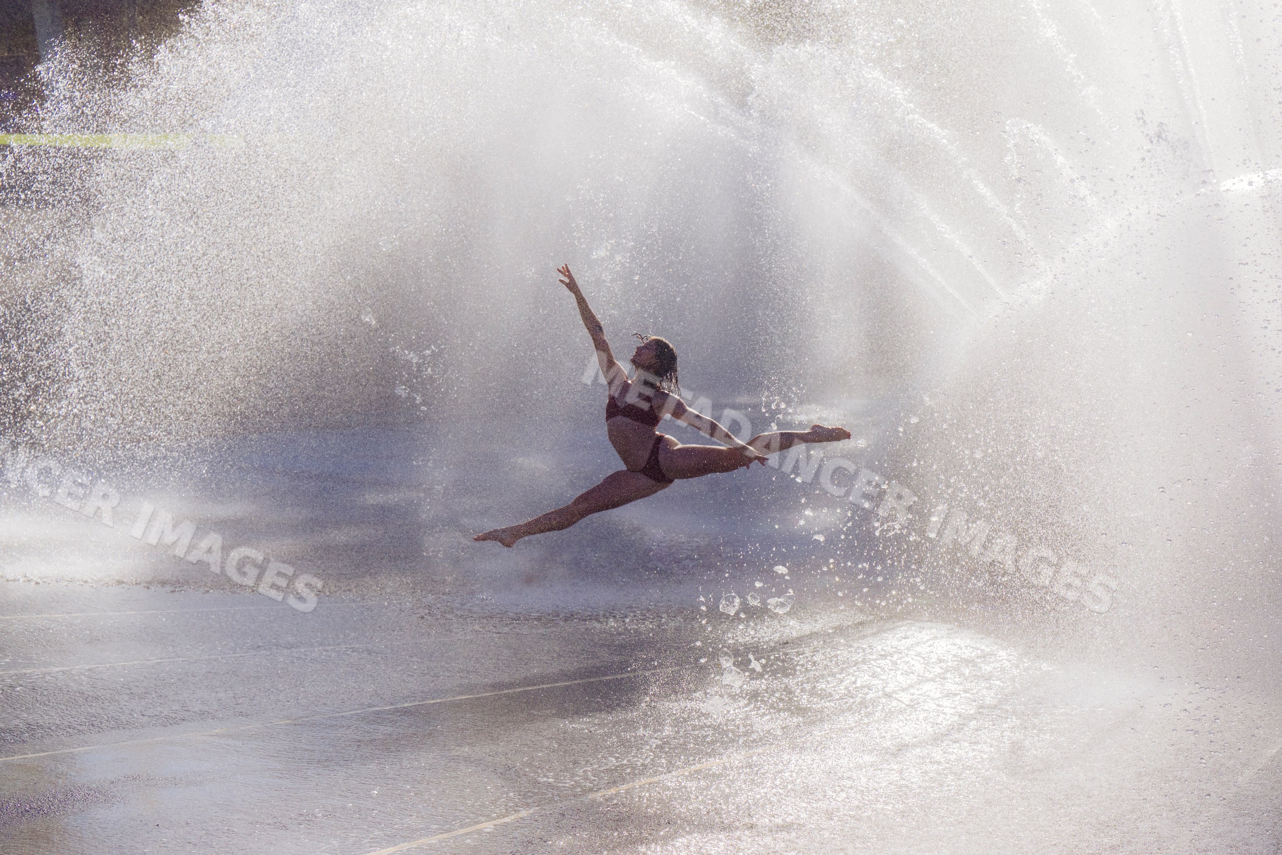 White woman performing a split leap through water spray